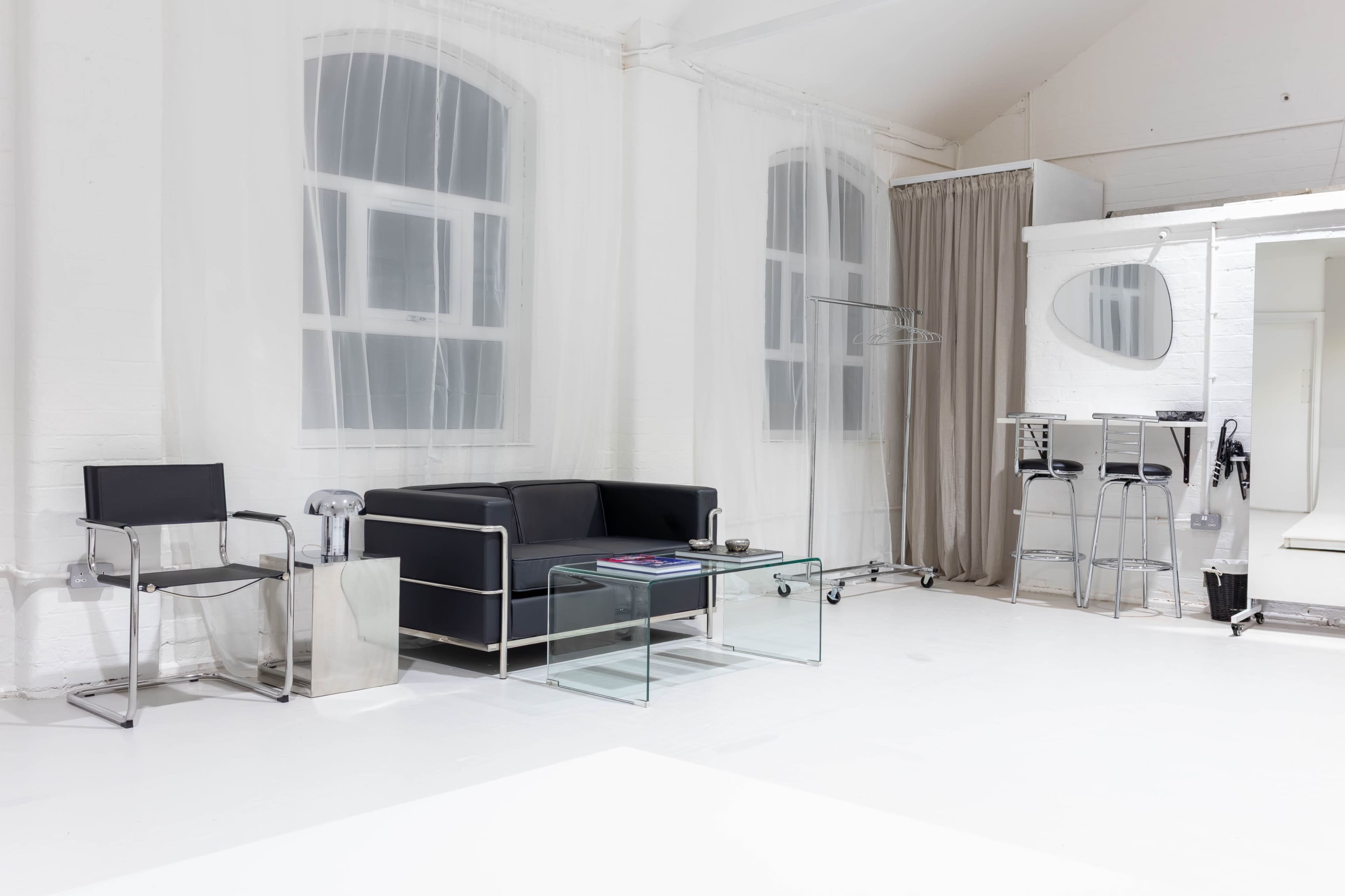 The scene features a minimalist interior with a black sofa, glass coffee table, and a combination of transparent and solid furniture, set against white walls and large windows.