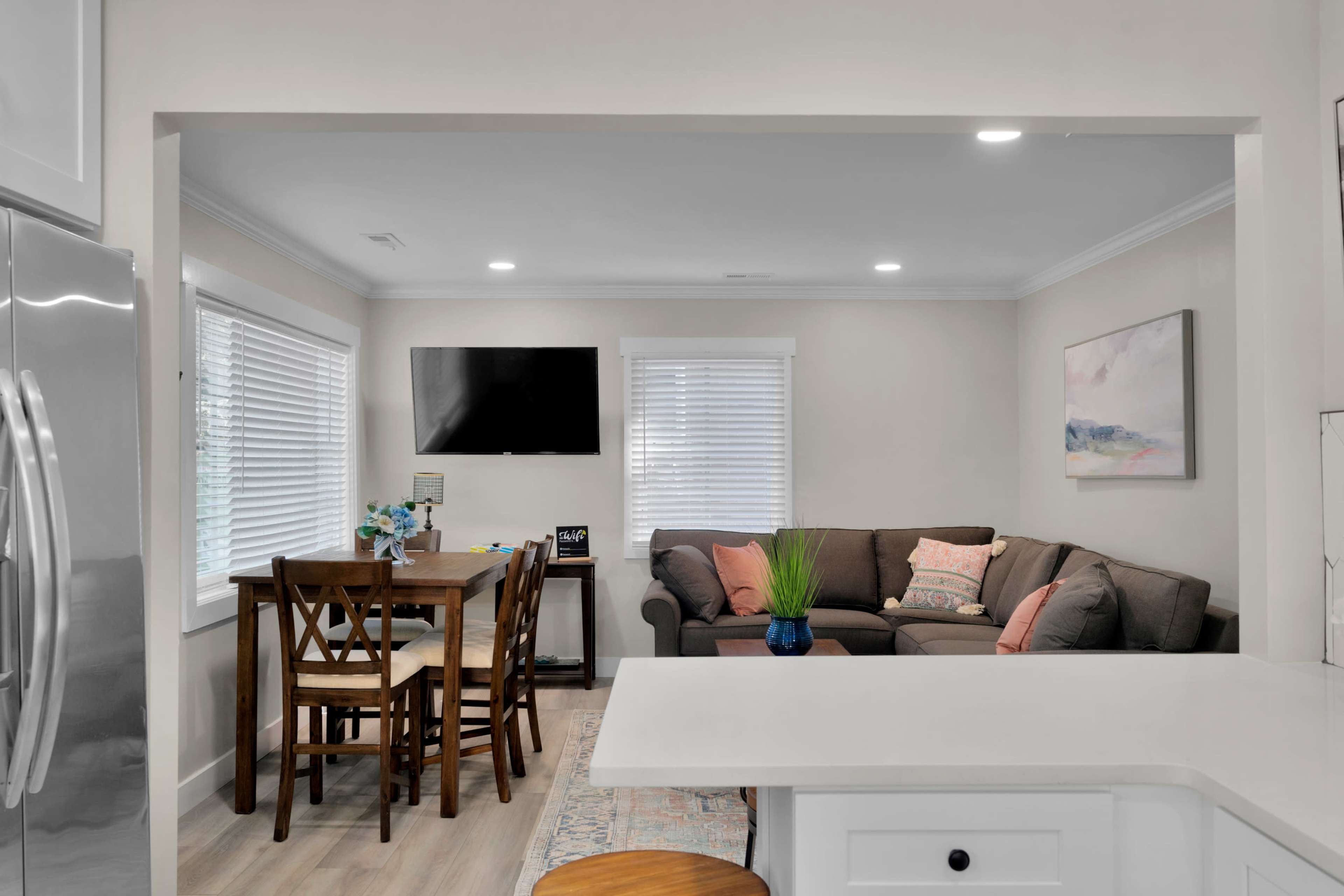 A modern, open-concept living area features a kitchen island overlooking a dining table and a seating area with a couch and wall-mounted TV.
