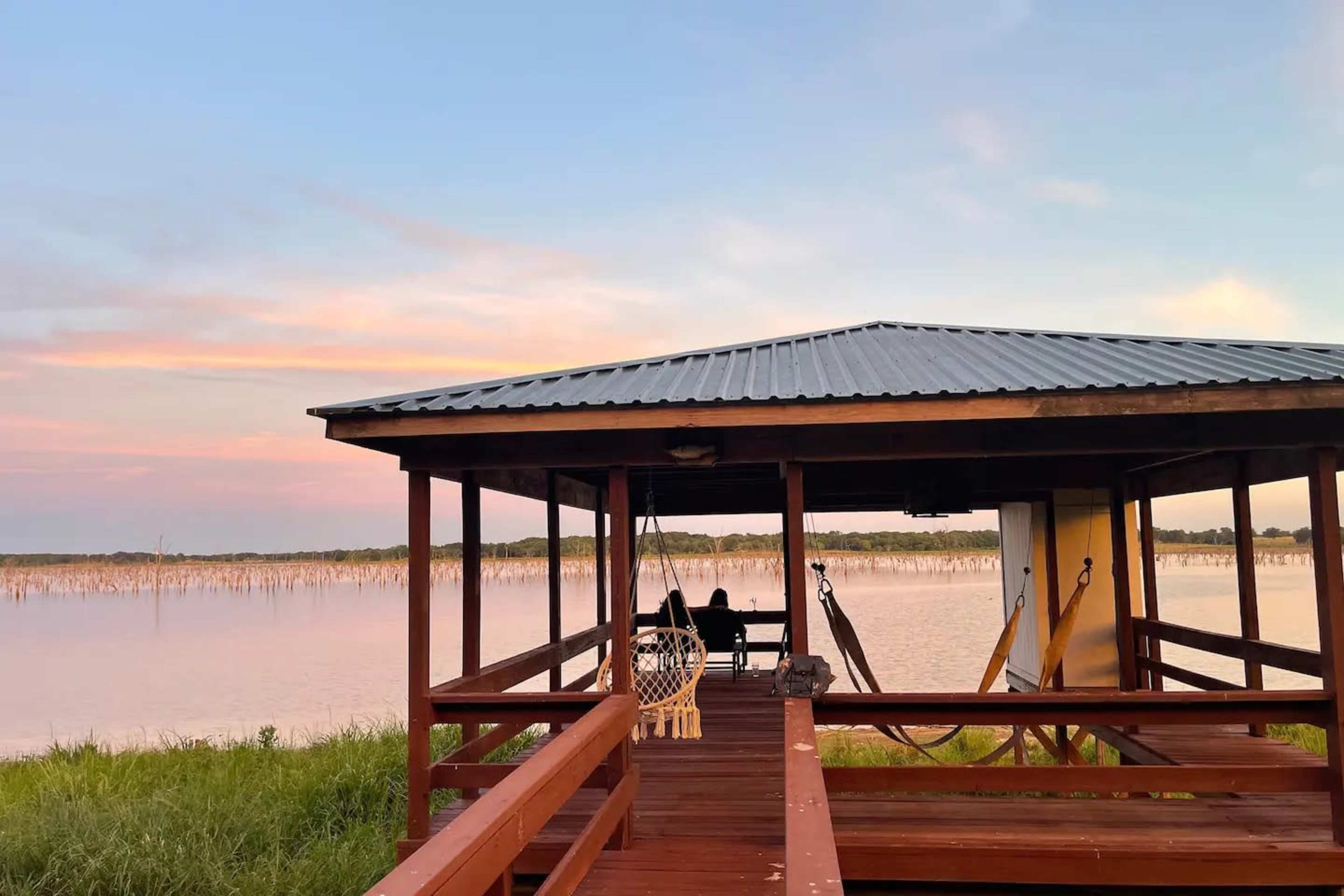 A wooden gazebo overlooking a calm body of water at sunset.