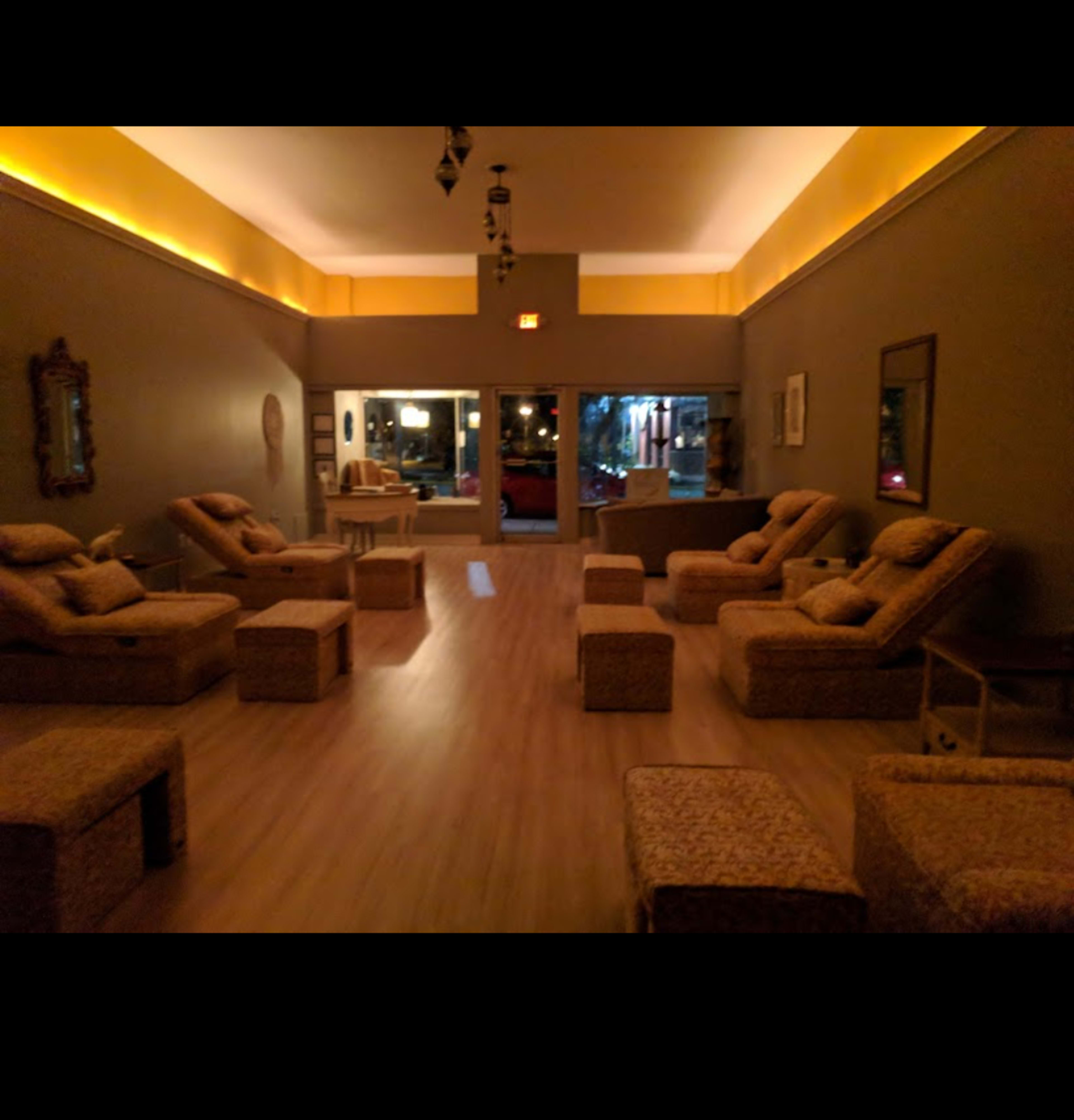 The interior of a spa features several wicker lounge chairs arranged in a spacious room with soft lighting and large windows.