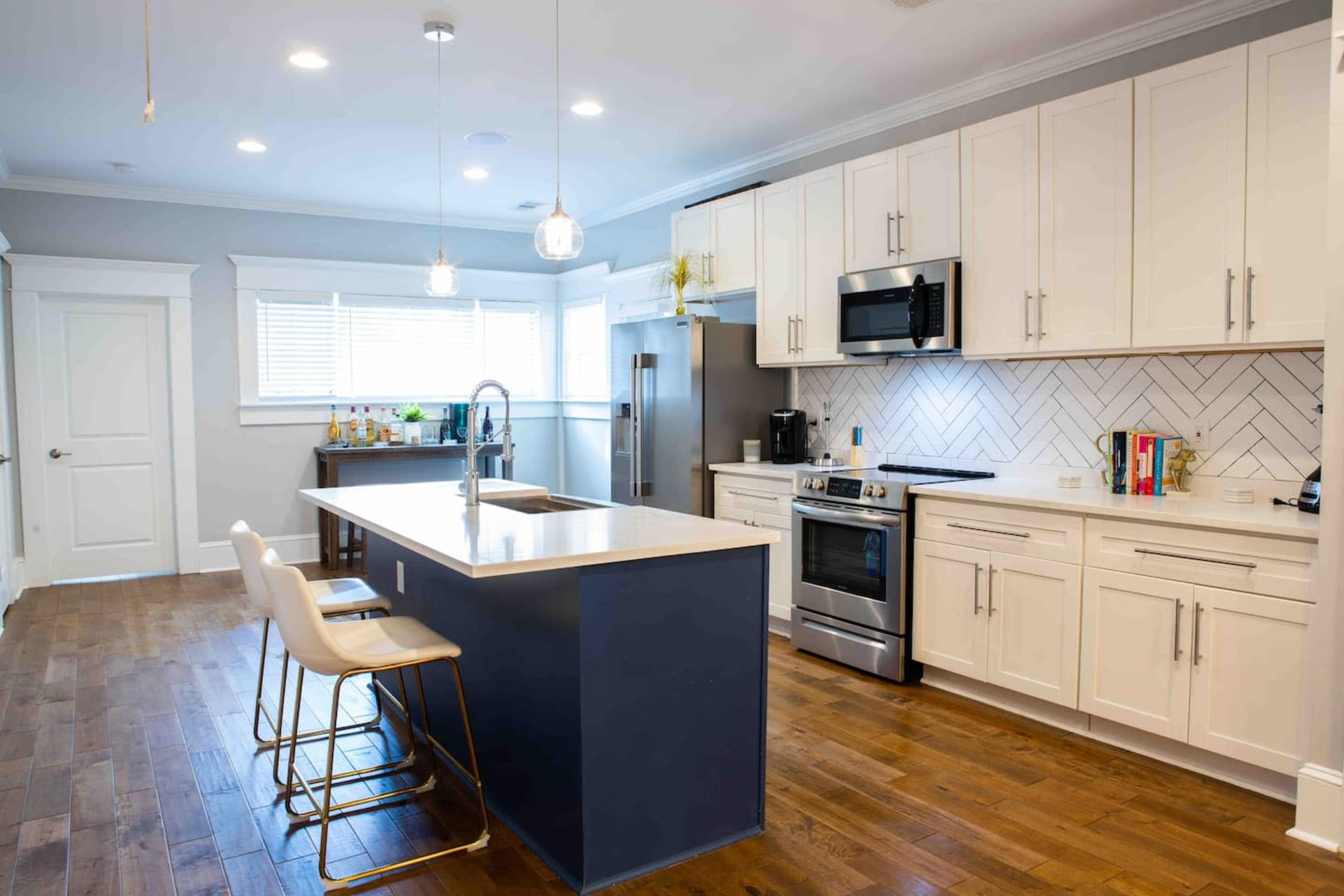 A modern kitchen features white cabinetry, stainless steel appliances, and a central island with bar stools, complemented by hardwood flooring.