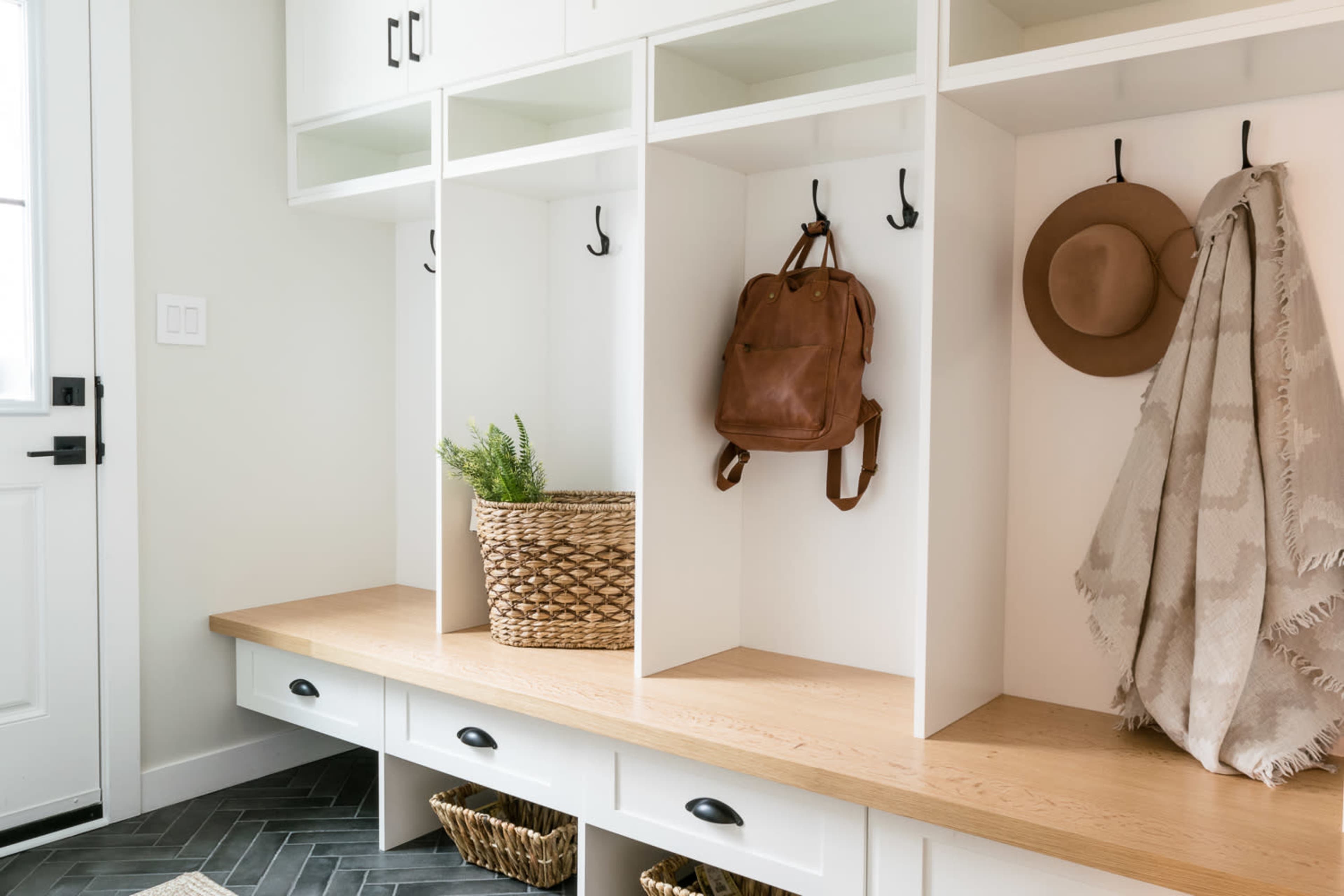 The image features a modern entryway with a wooden bench, cubby storage, hooks for items, and decorative baskets.