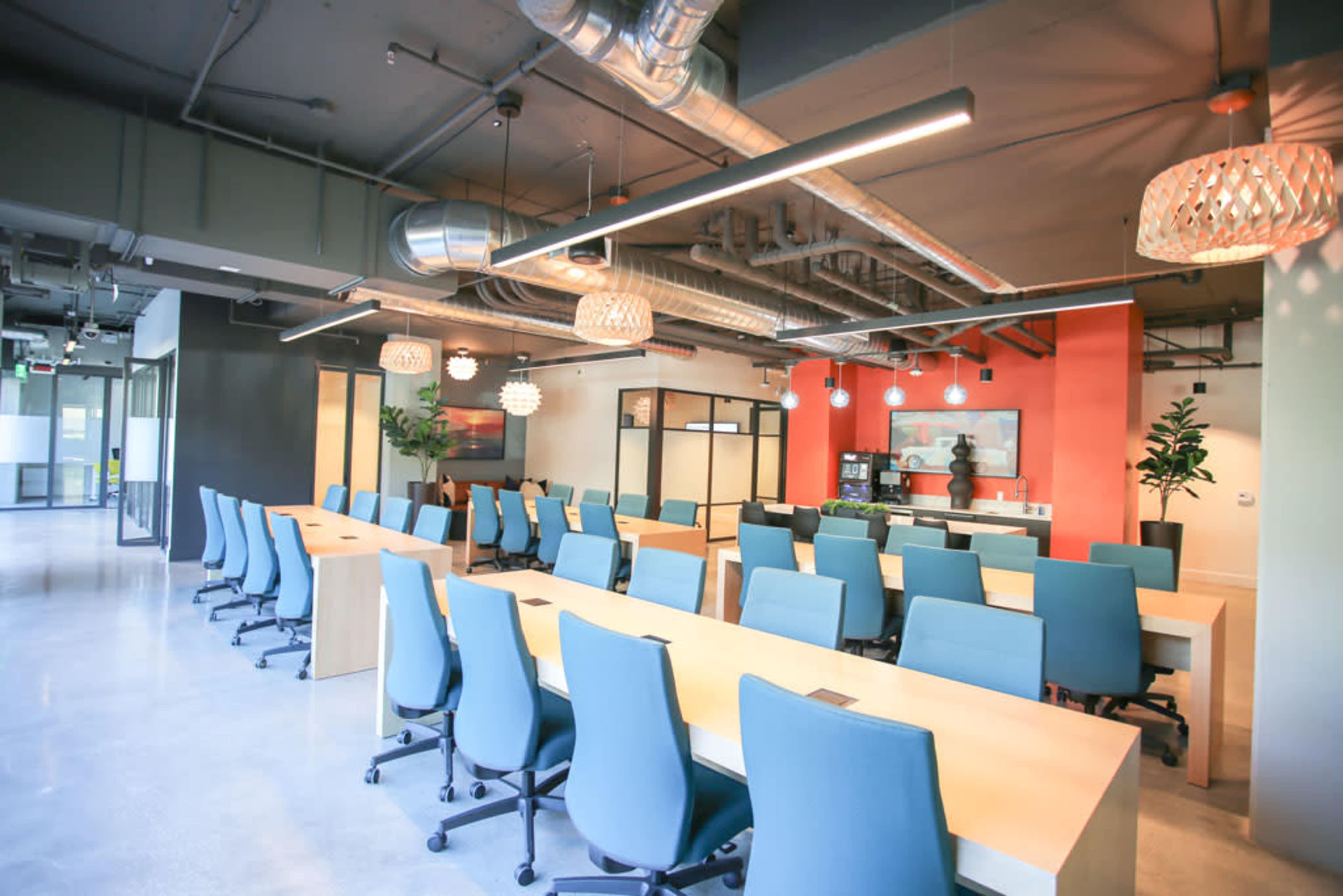 A modern office space features long tables with blue chairs, surrounded by contemporary decor and large windows.
