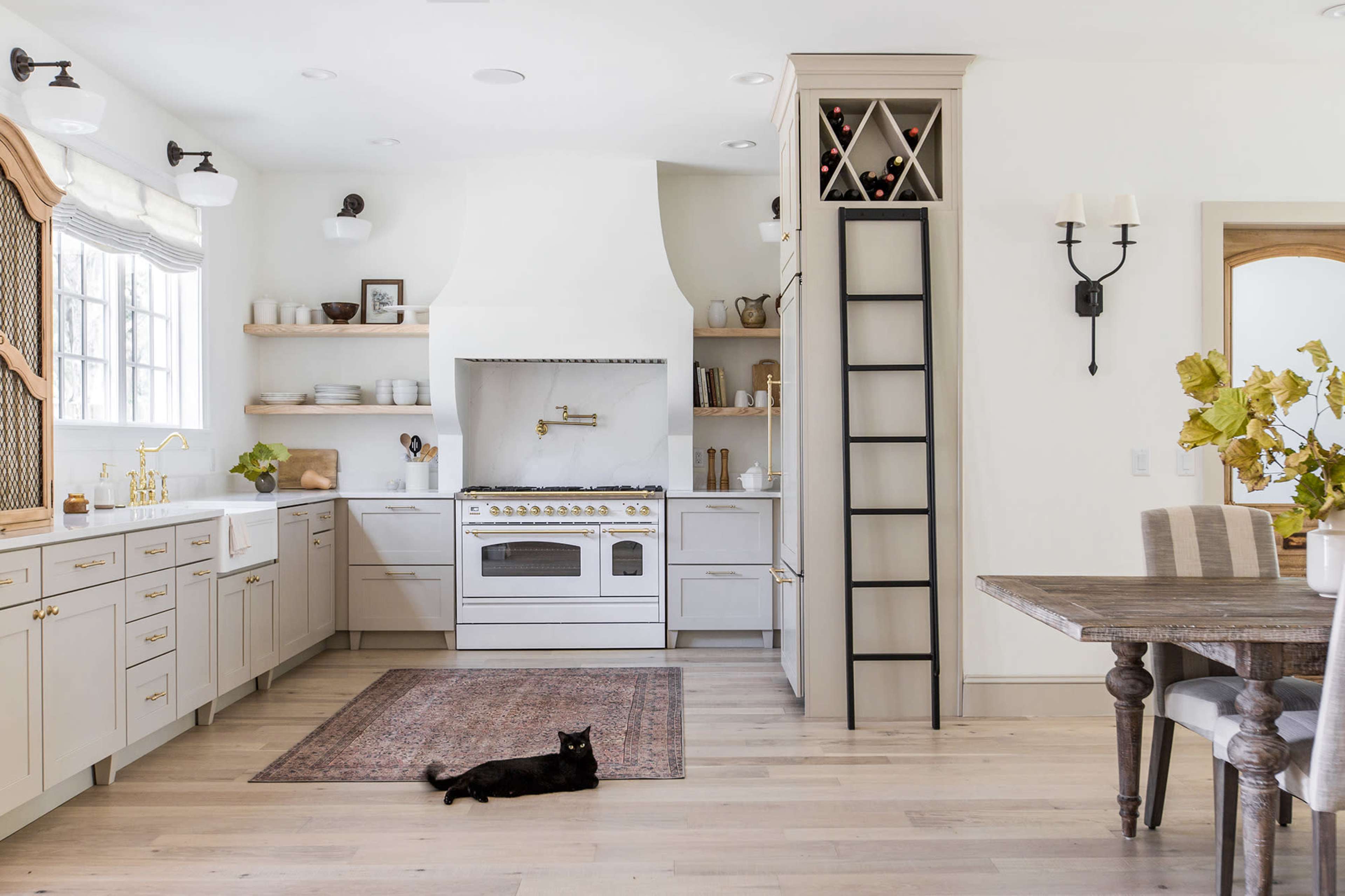 A modern kitchen features light-colored cabinets, an island with a stovetop, and a black cat lounging on a rug.
