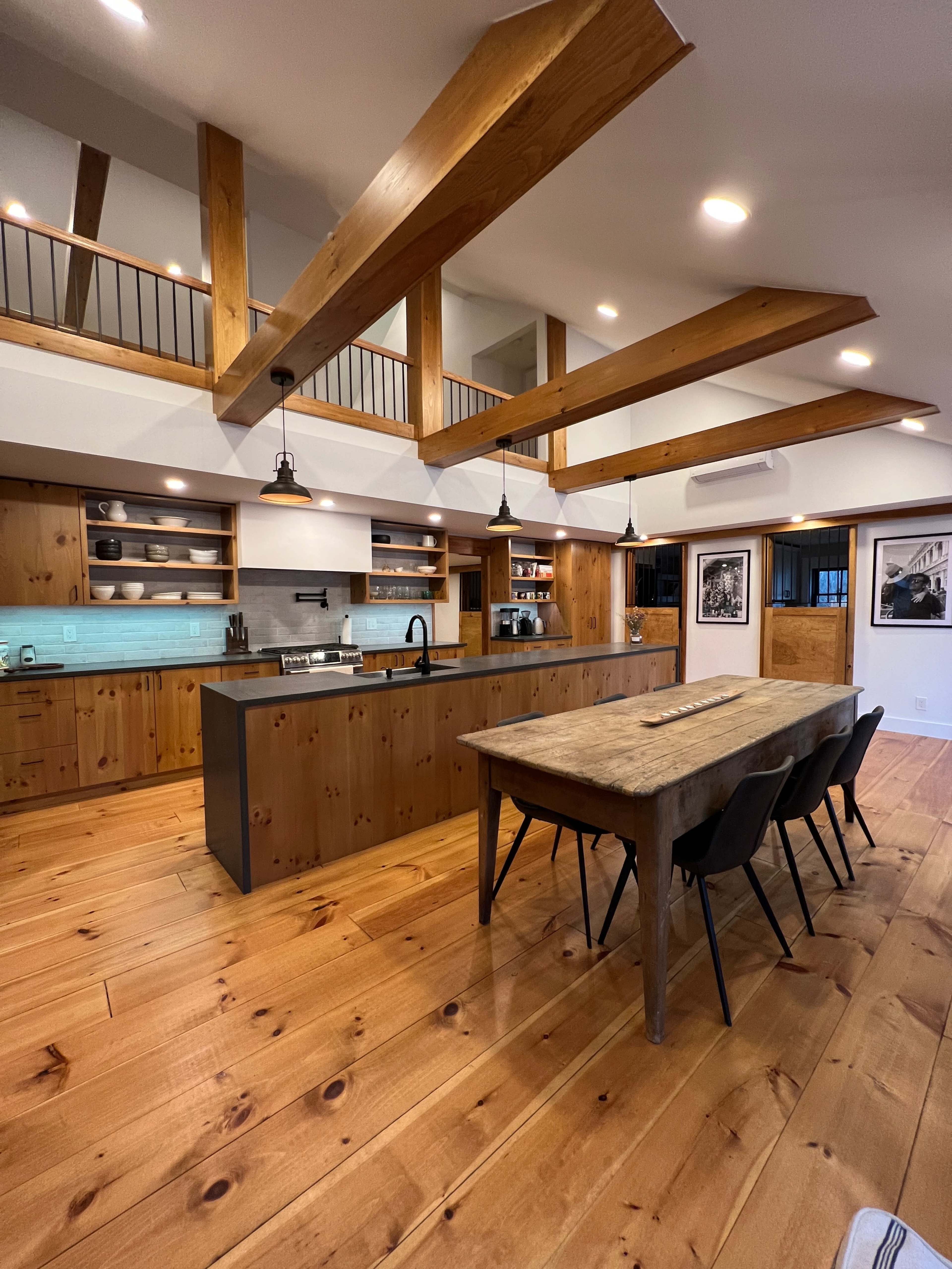 A wooden kitchen and dining area with exposed beams, a large island, a dining table, and modern black chairs.