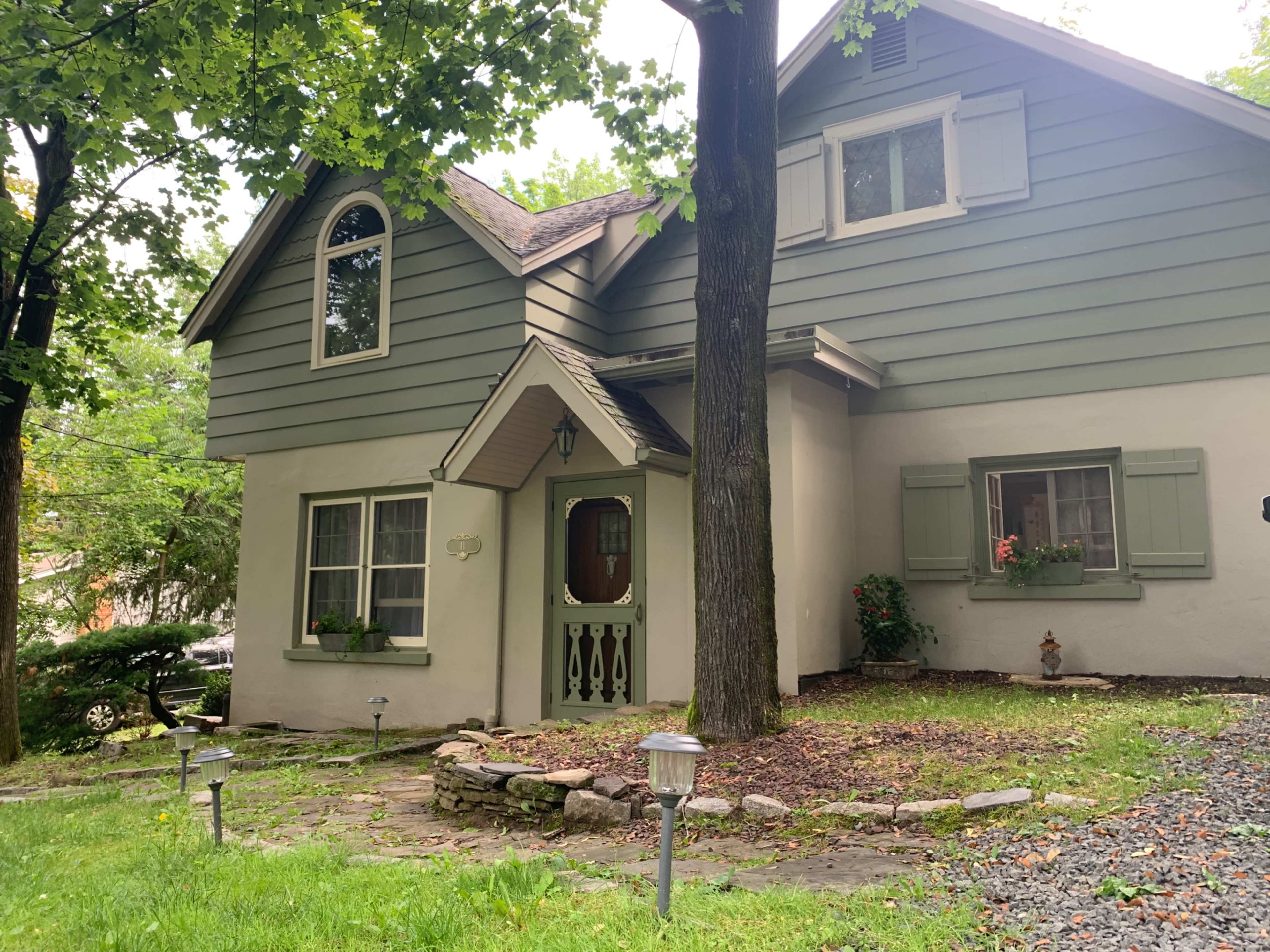 A two-story house with green siding, decorative shutters, and a landscaped front yard featuring stone pathways and garden lights.