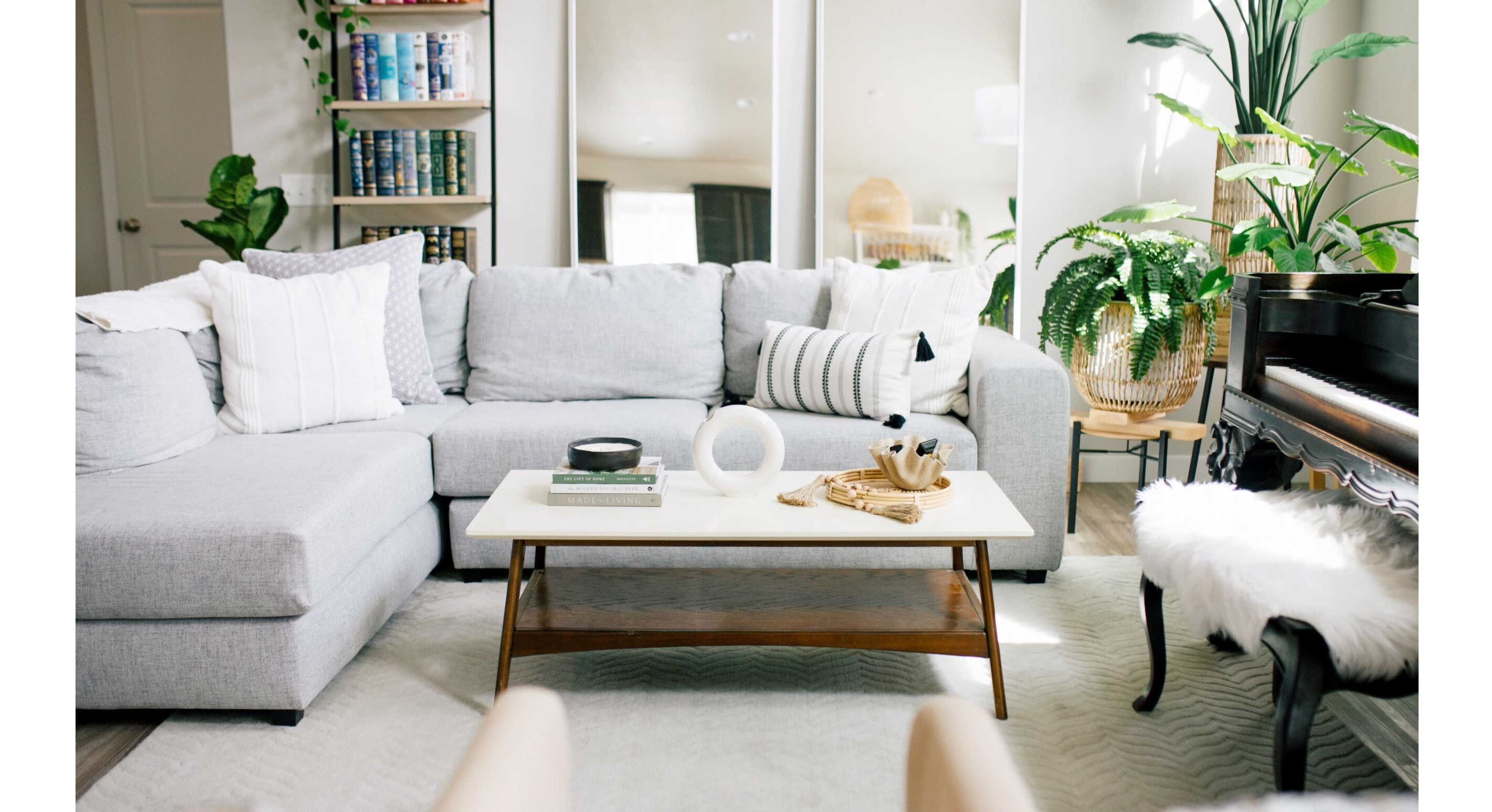 A modern living room featuring a gray sectional sofa, a coffee table with decor items, and a piano surrounded by plants.