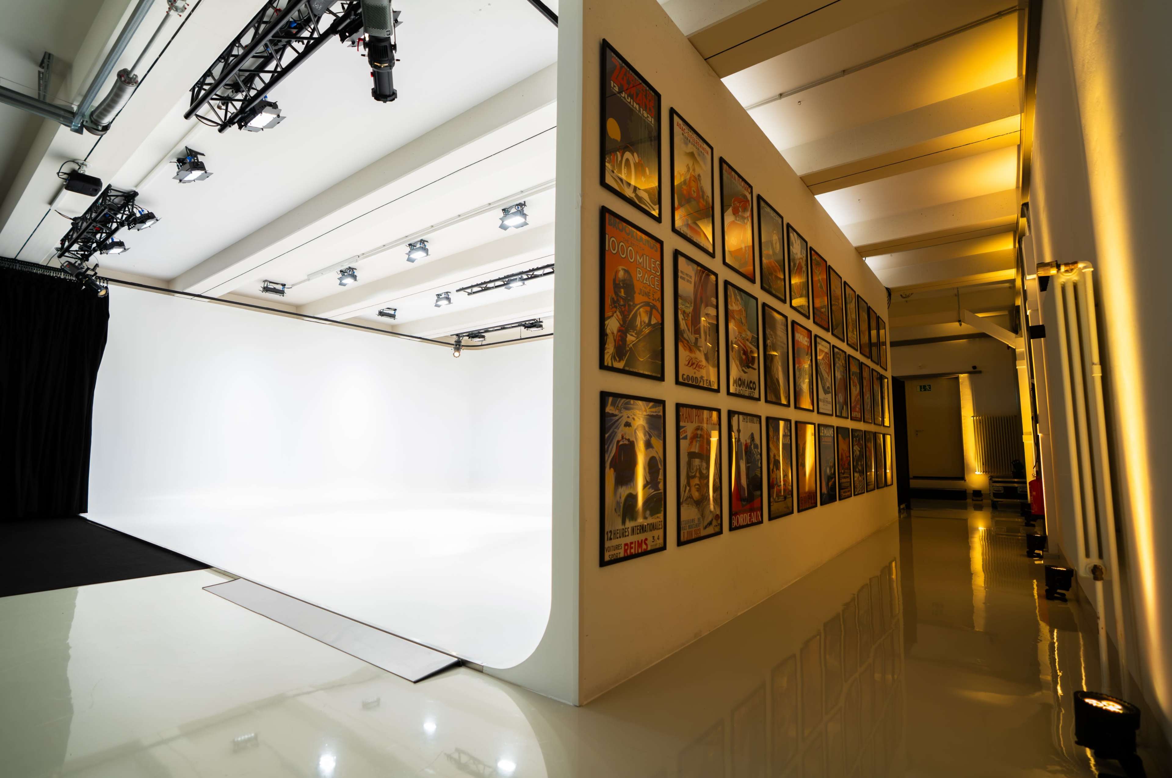 The image shows a studio space featuring a white backdrop and a wall adorned with various framed posters.