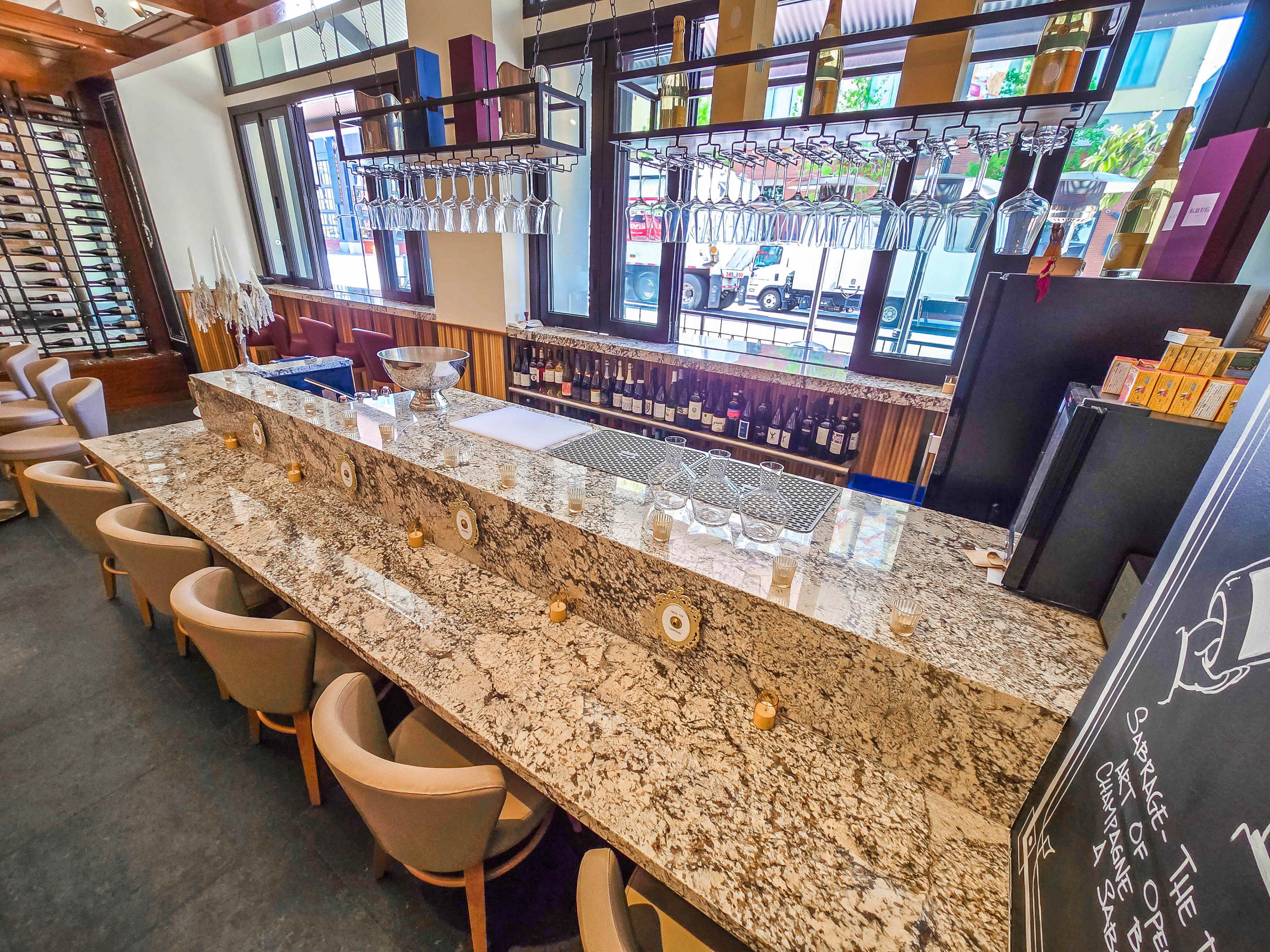 The image shows a well-organized bar area with a granite countertop, wine bottles on display, and chairs lined up along the bar.