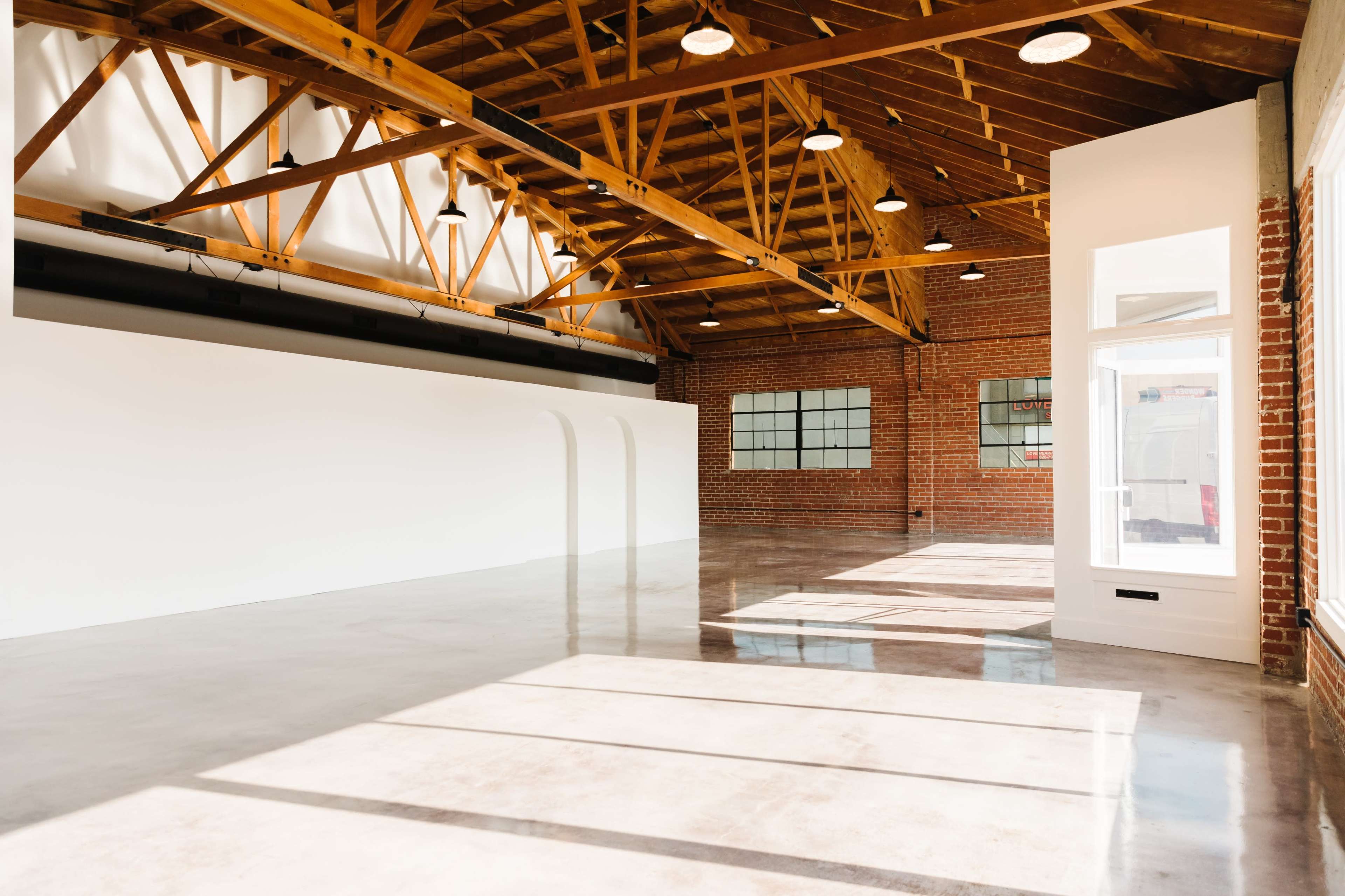 A spacious interior with exposed wooden beams, large windows, and polished concrete flooring.
