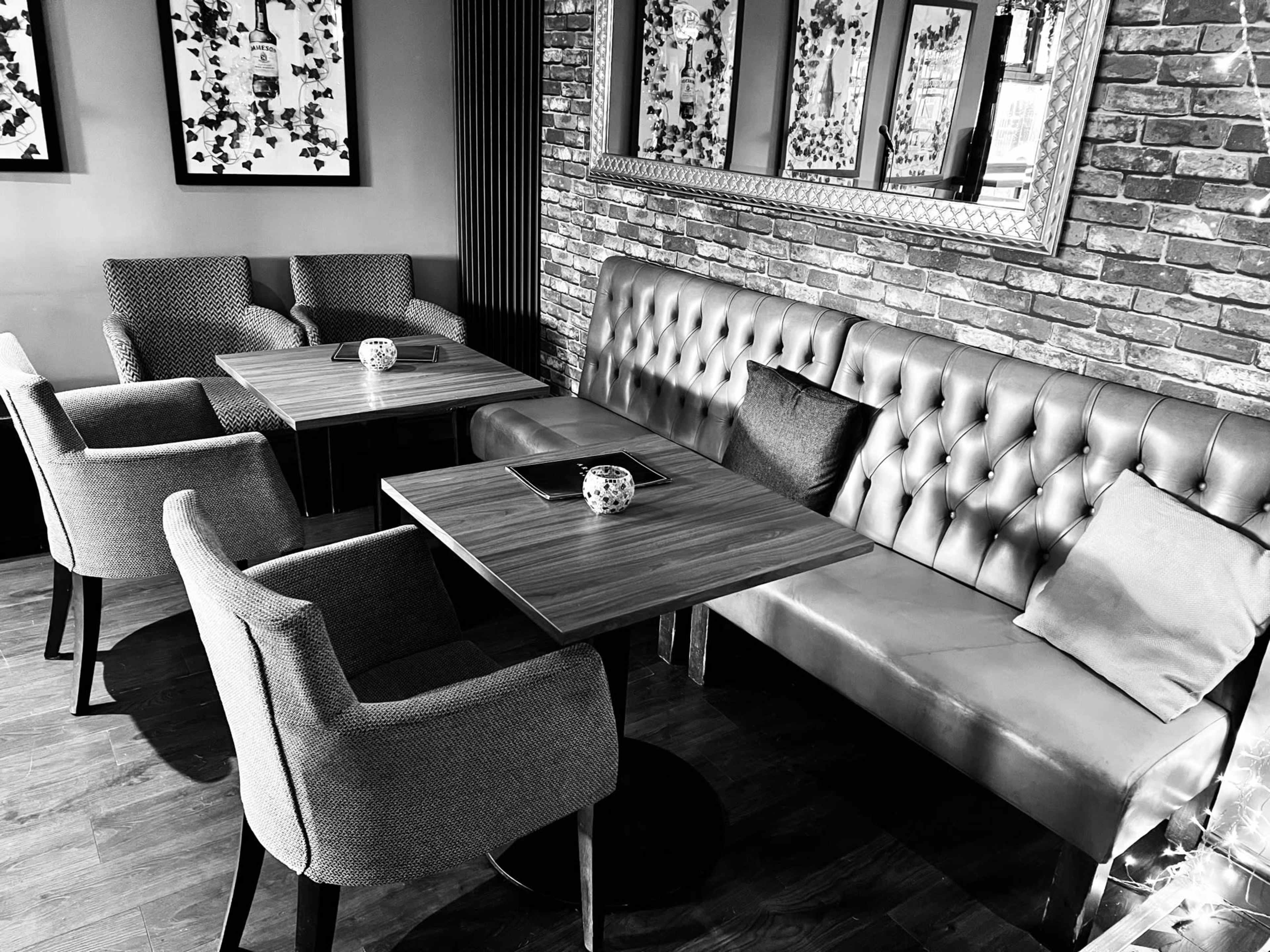 The image shows a cozy seating area with two tables and a mix of upholstered chairs and a tufted bench against a brick wall, framed by decorative mirrors.