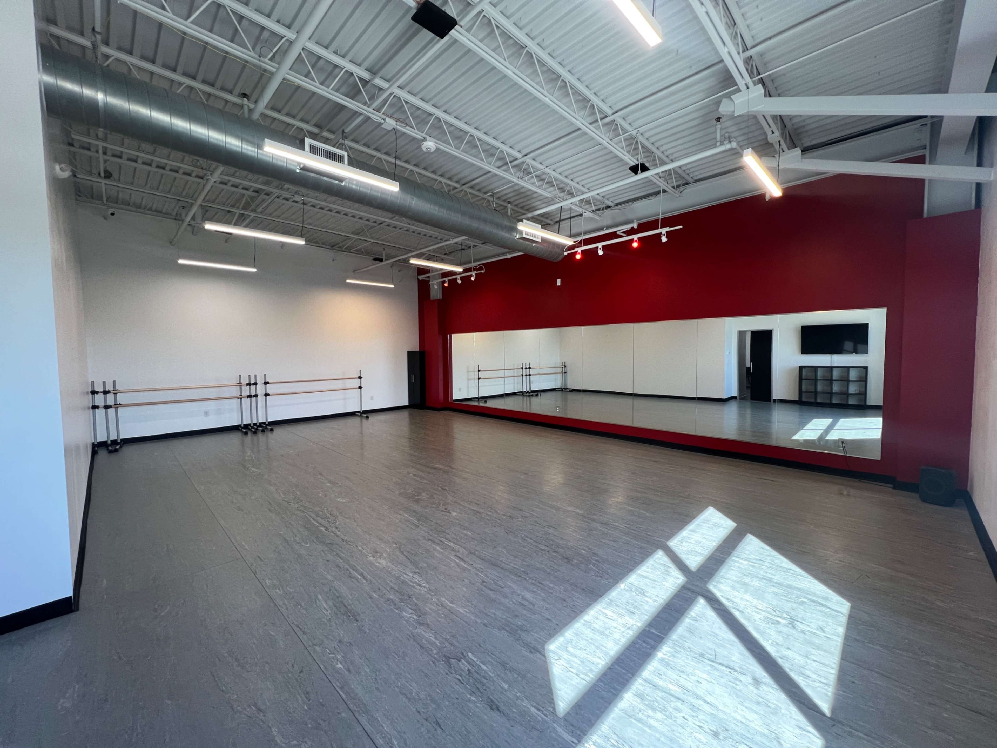 The image shows a spacious dance studio with wooden ballet bars along one wall and a large mirror reflecting the room's interior.
