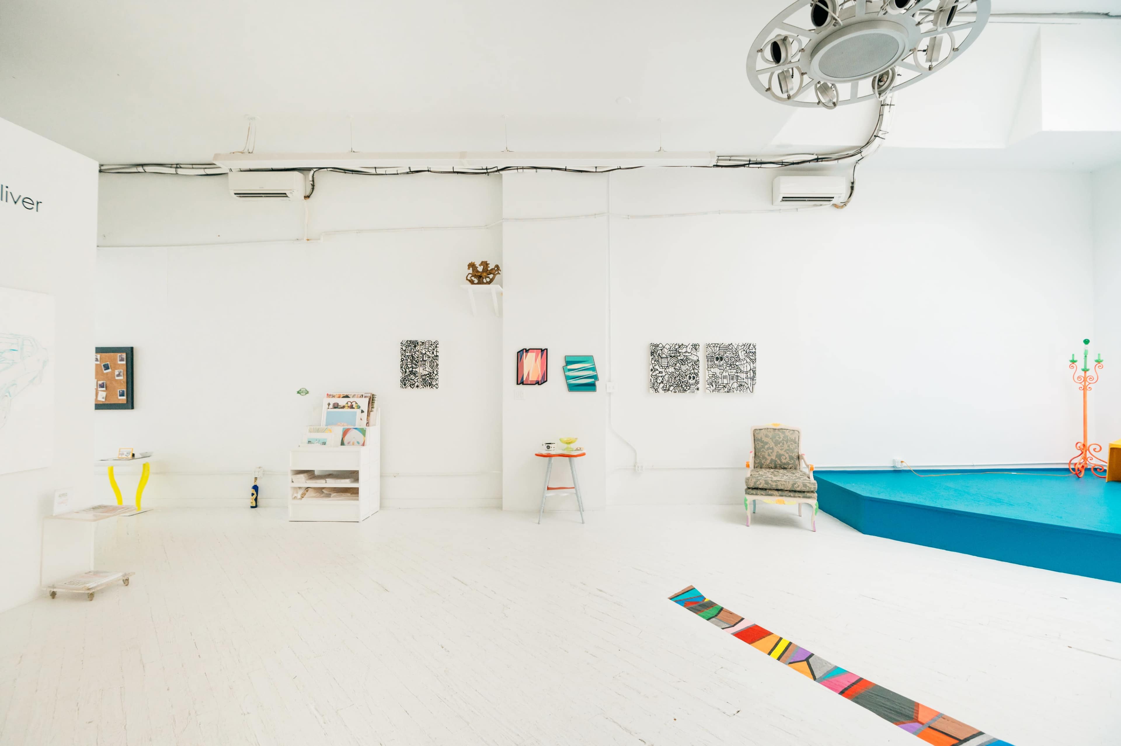 A modern art gallery featuring a white space with various artworks displayed on the walls and a colorful floor installation.