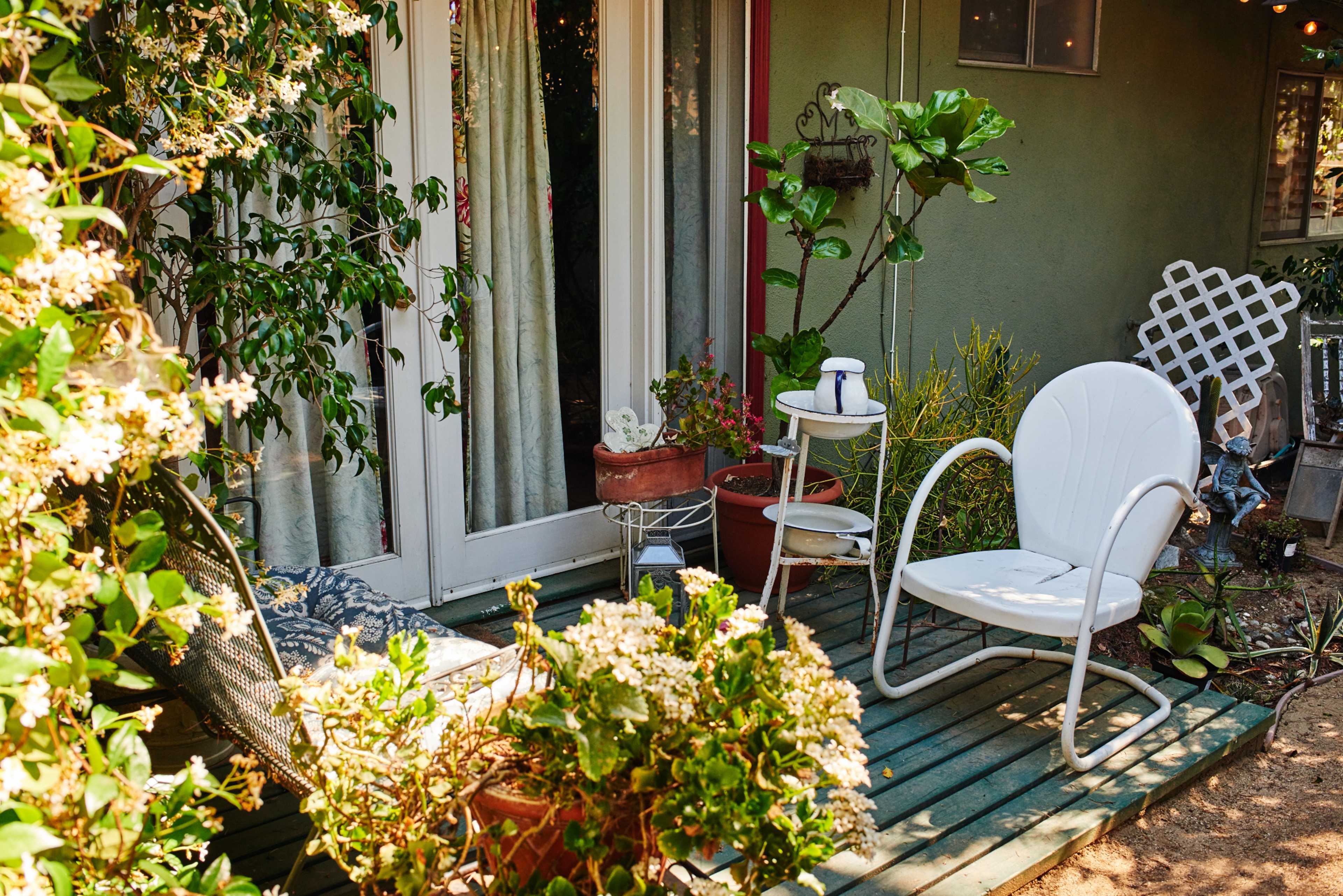 A white chair and a small side table are situated on a wooden deck surrounded by various potted plants.