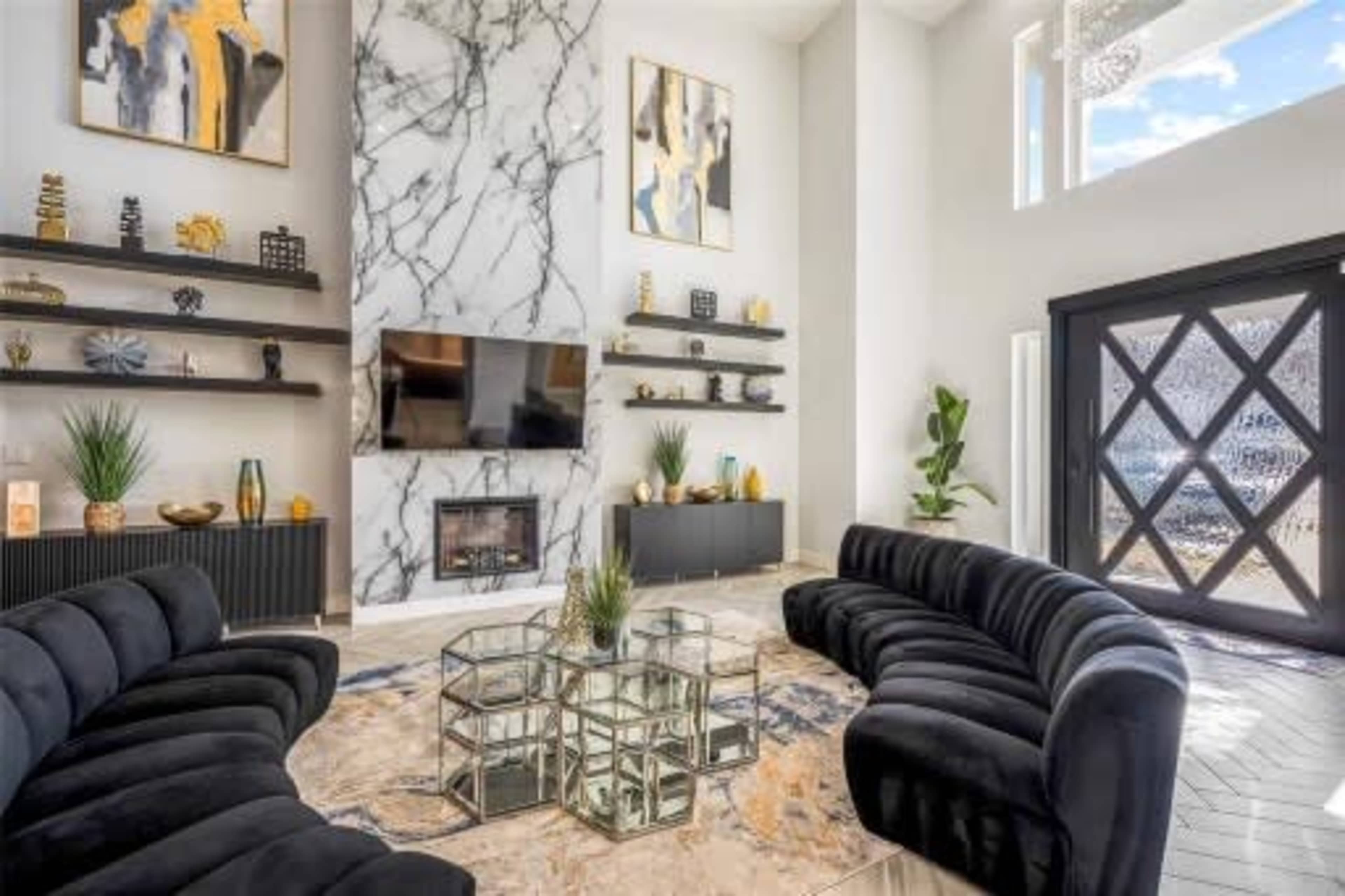 A modern living room features a marble accent wall with a mounted TV, sleek black furniture, and decorative shelves.