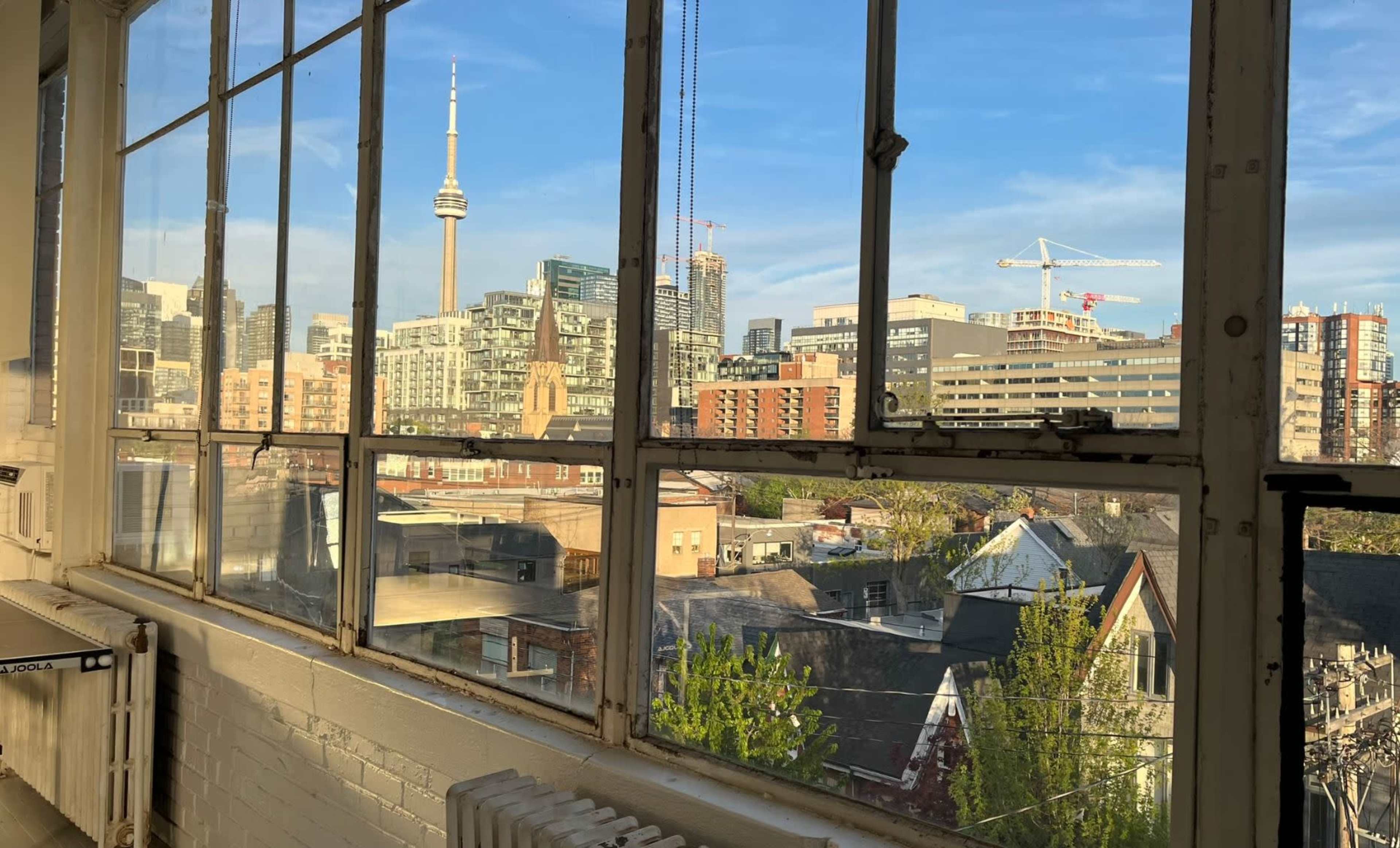 A view from a window overlooking a cityscape with the CN Tower in Toronto, surrounded by various buildings and rooftops.