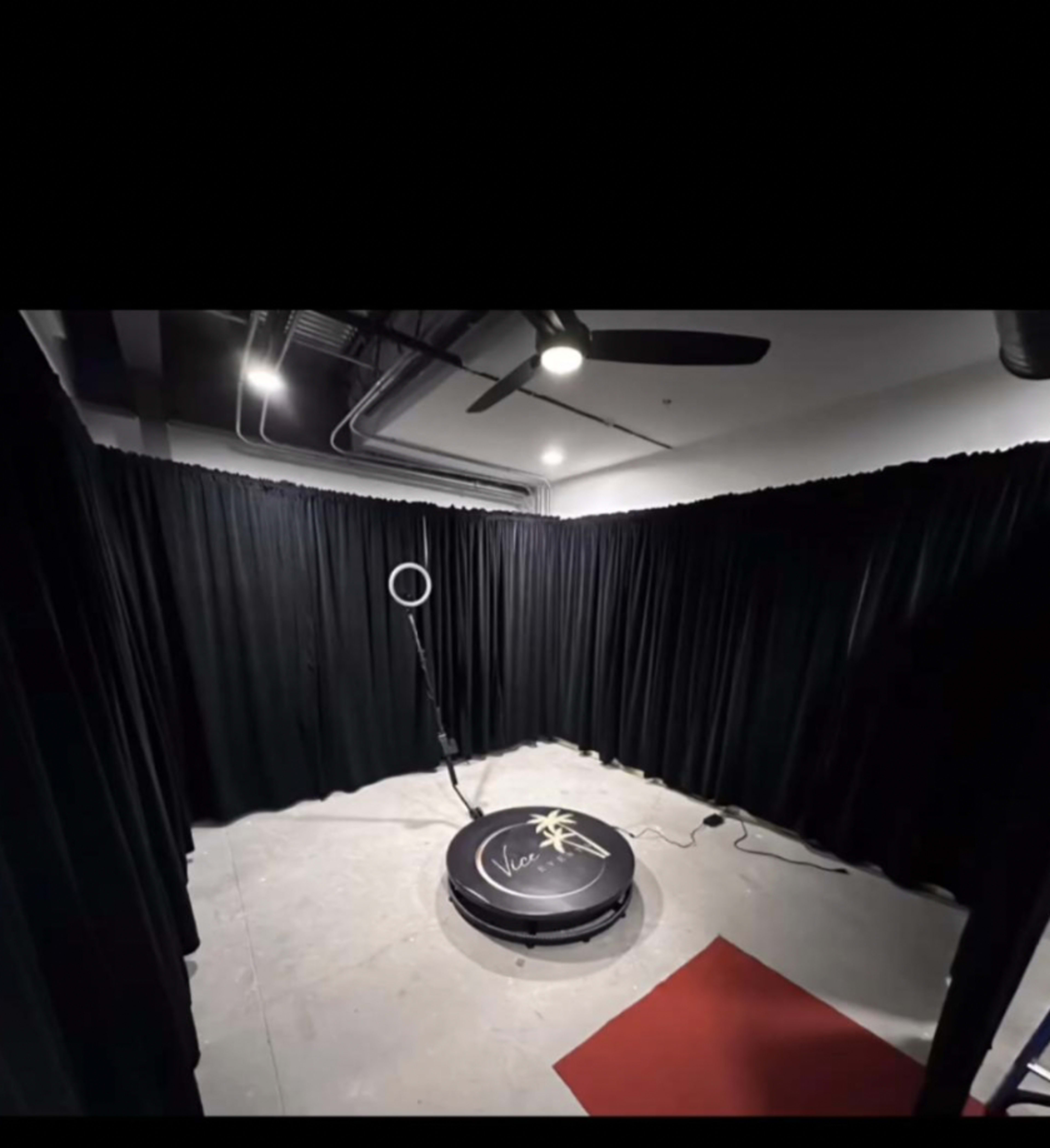 A partially enclosed space with black curtains, a circular platform in the center, and a ring light on a stand.