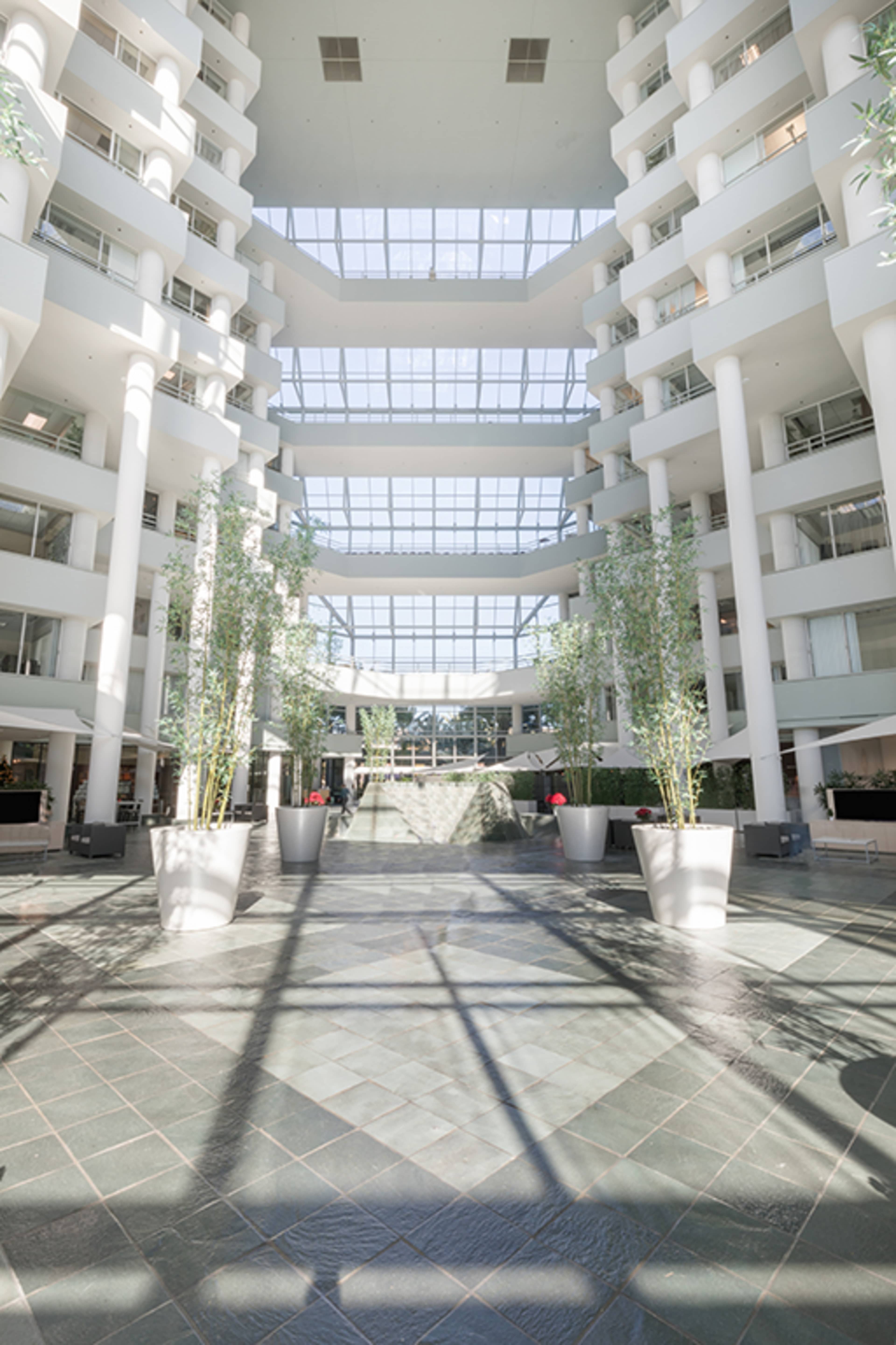 A spacious atrium with tall white columns, glass ceilings, and potted plants.