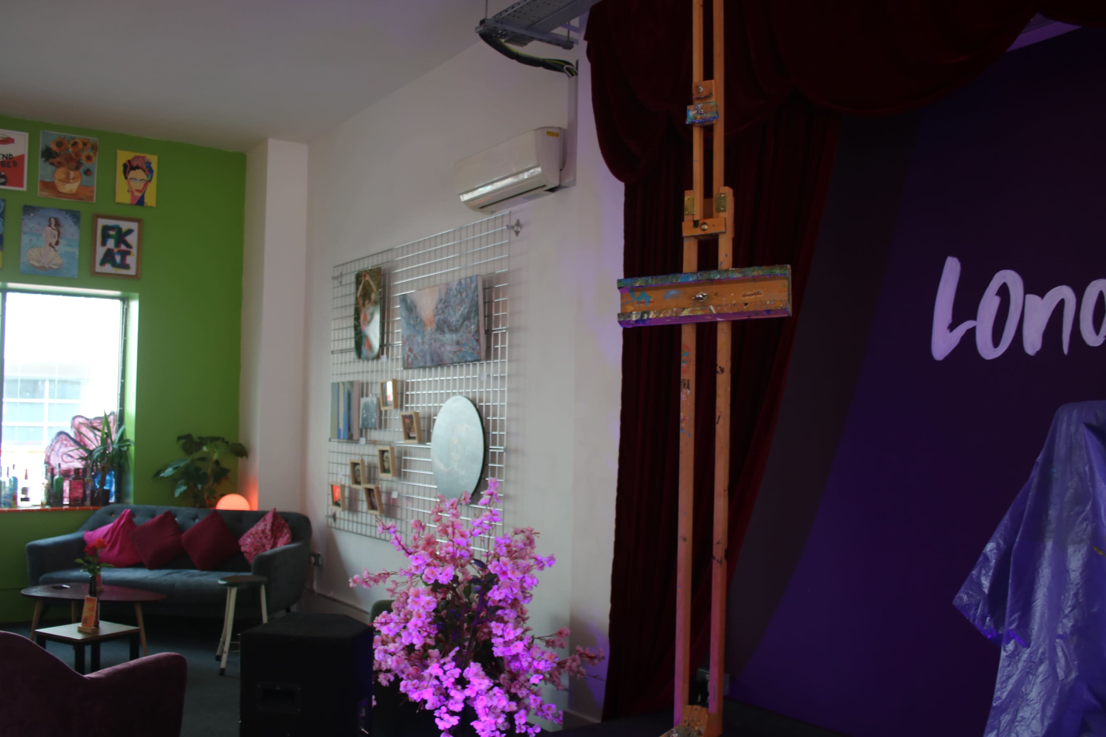 The image shows a colorful interior space featuring an easel, a mirrored wall display, a floral arrangement, and a curtain backdrop.