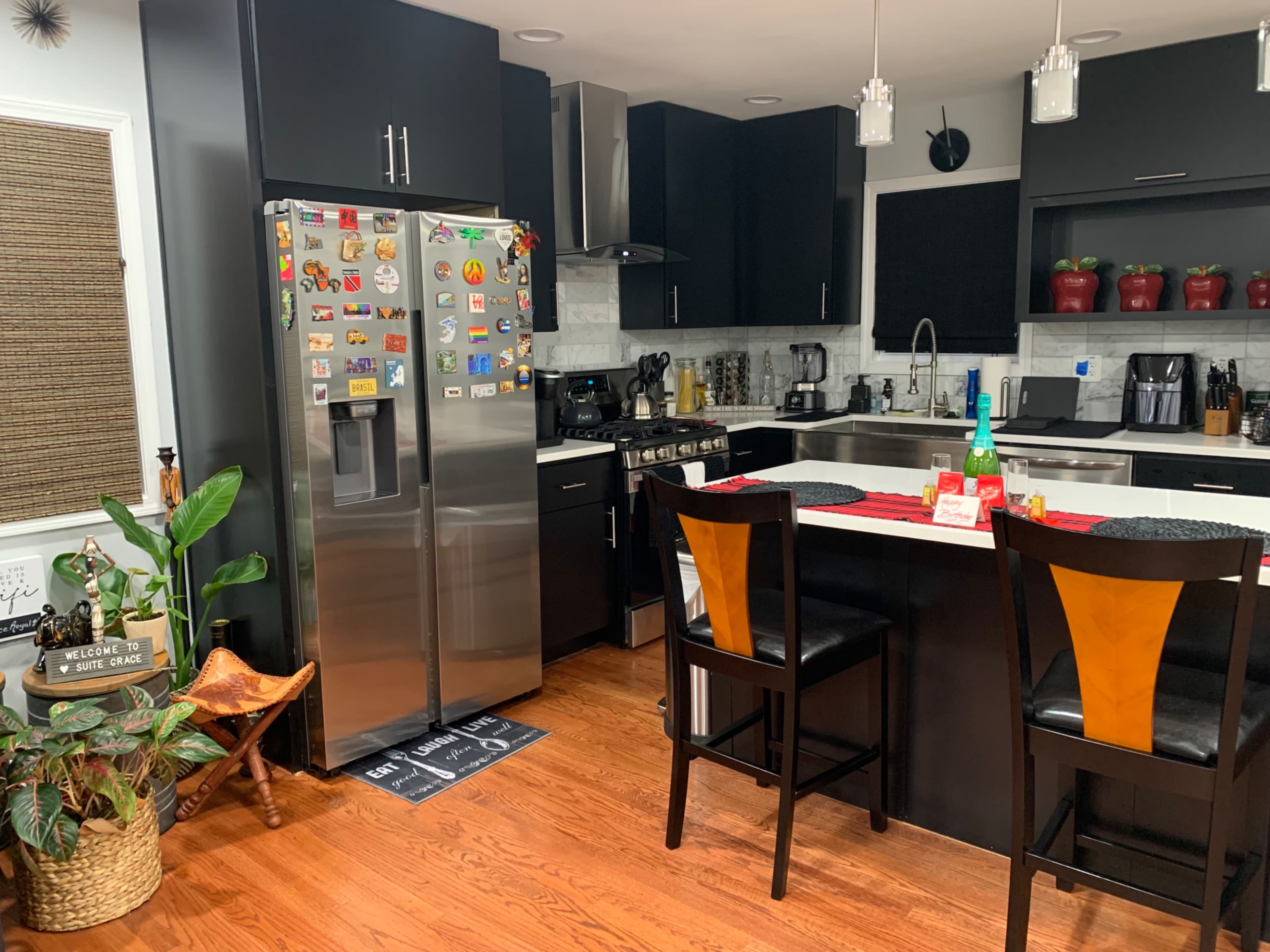 The image features a modern kitchen with black cabinetry, stainless steel appliances, and a dining area with two high-backed chairs.