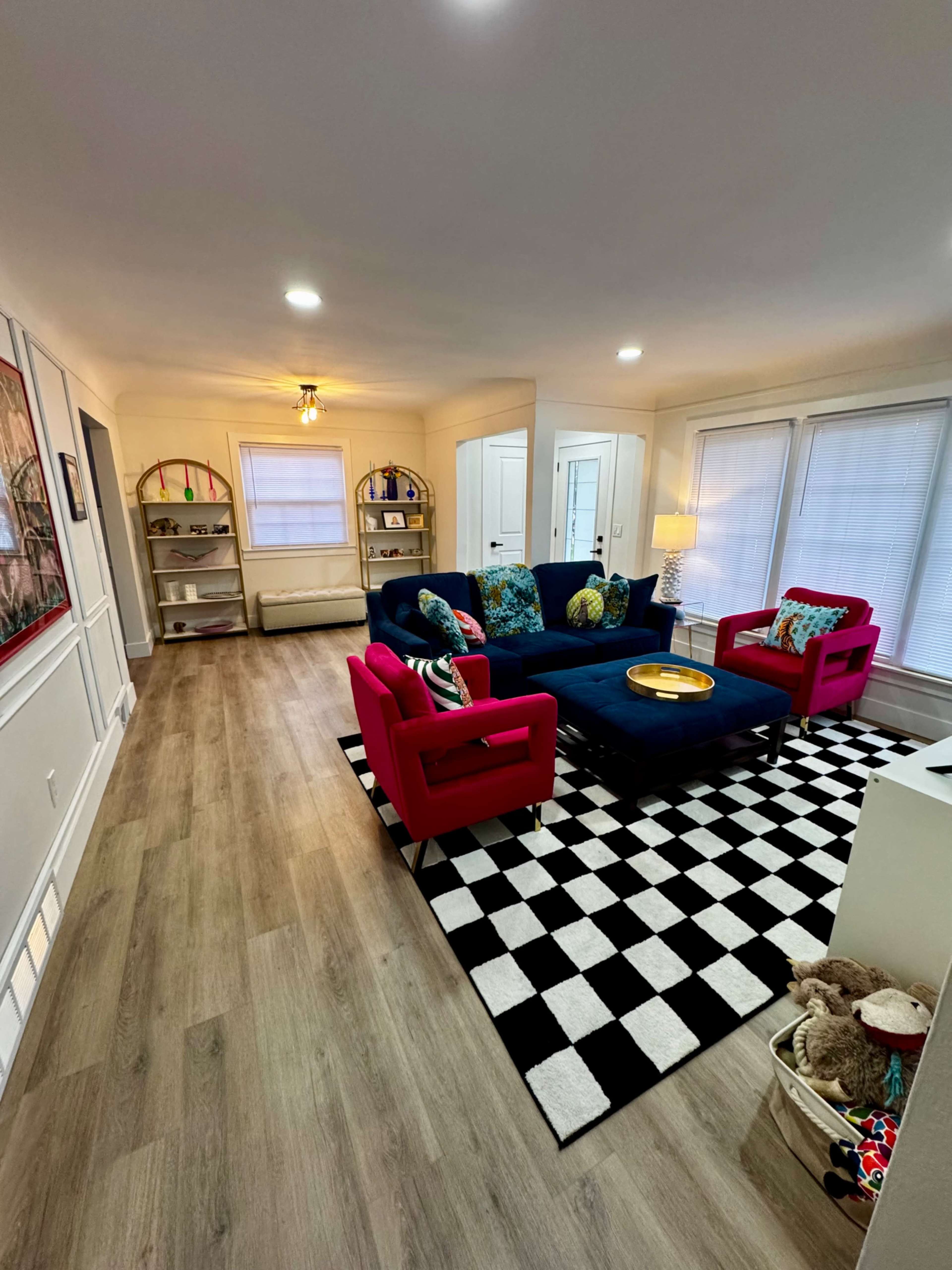 The image shows a modern living room with a navy blue sofa and two red armchairs on a black-and-white checkered rug.