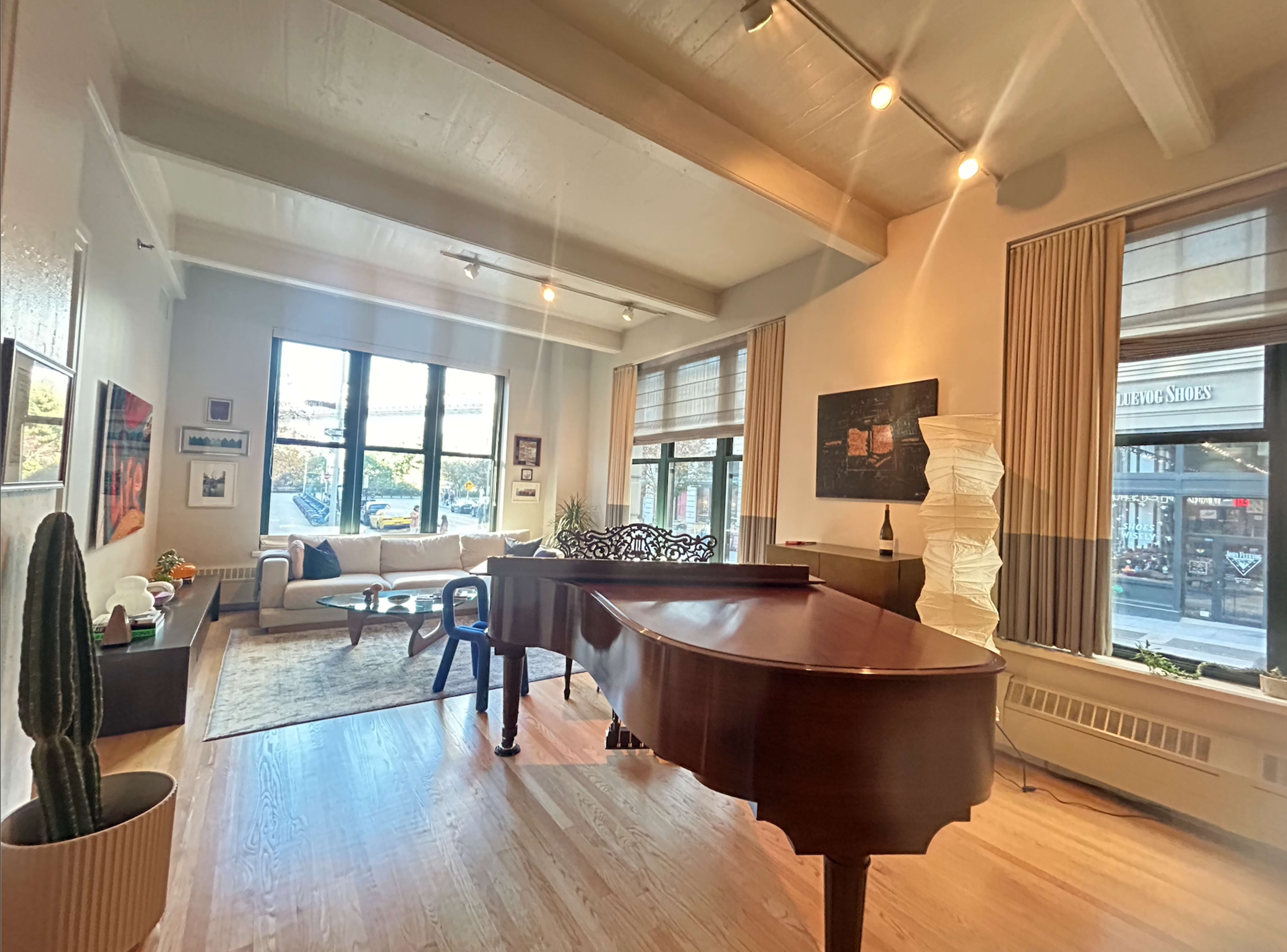 A spacious living room features a grand piano, large windows, a cozy seating area, and a modern decor.