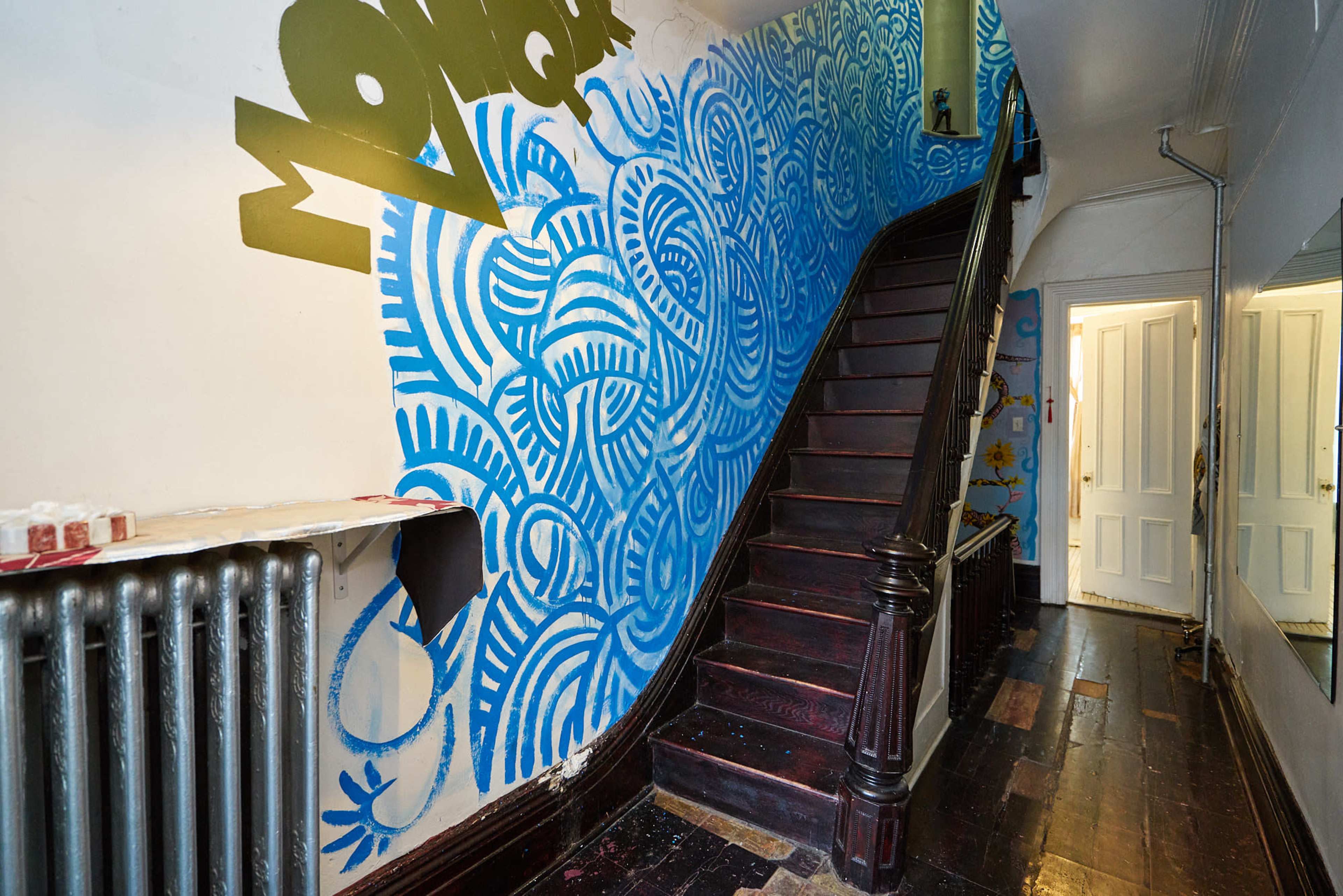 The image shows a stairway with a blue and white decorative mural on the wall and a wooden railing leading to an upper floor.