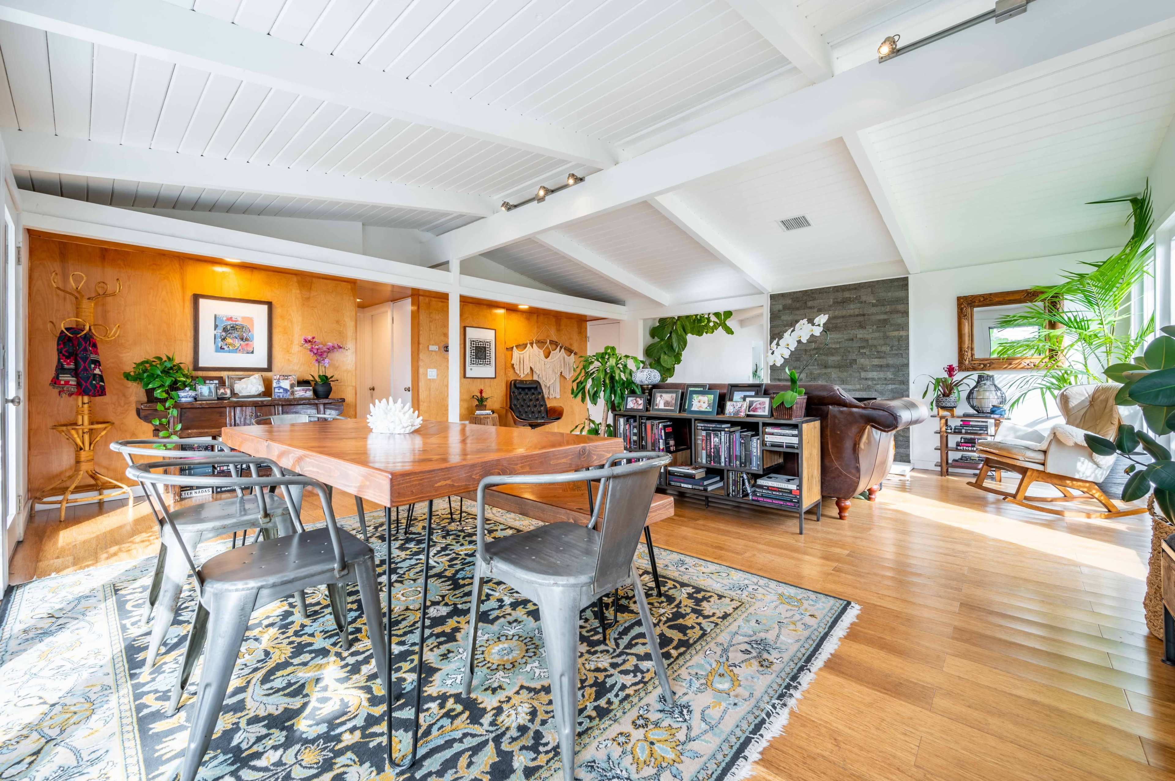 A spacious room features a wooden dining table surrounded by metal chairs, with plants and artwork enhancing the decor.