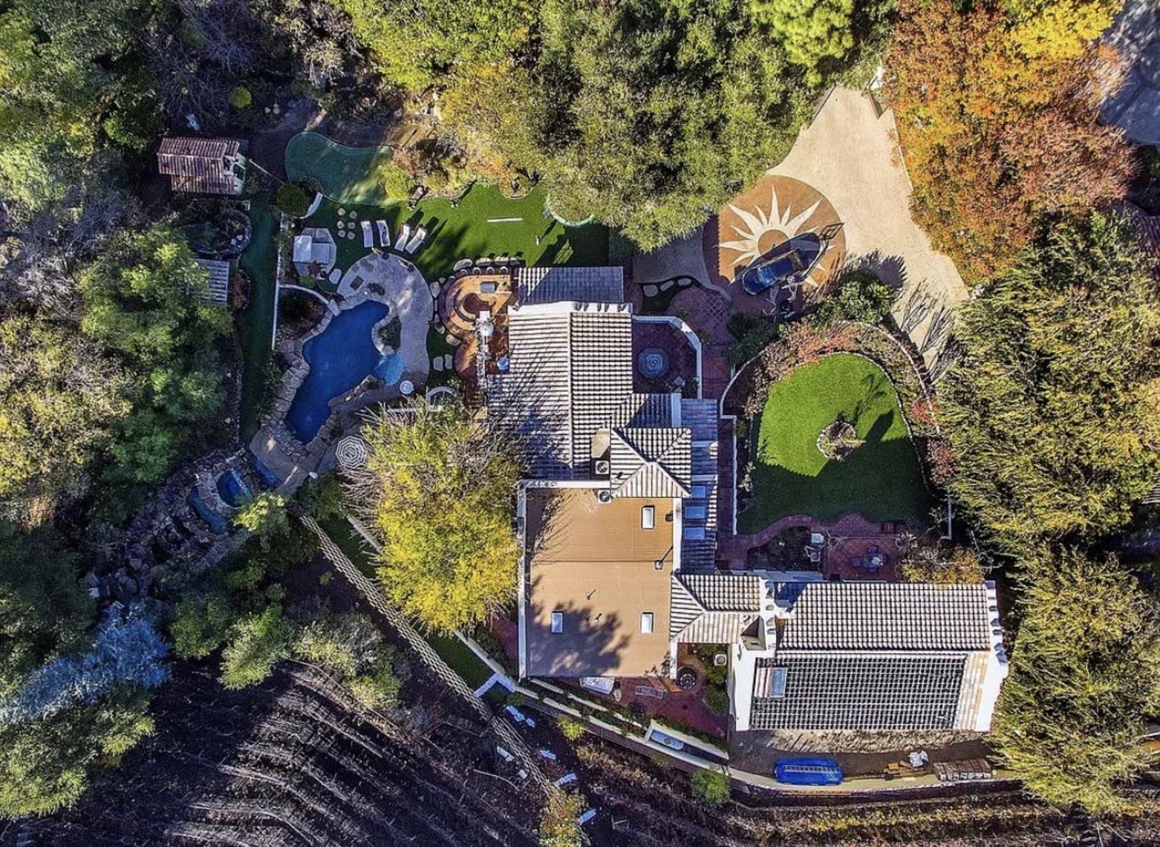 An aerial view of a large estate featuring landscaped gardens, a swimming pool, and various outdoor seating areas.
