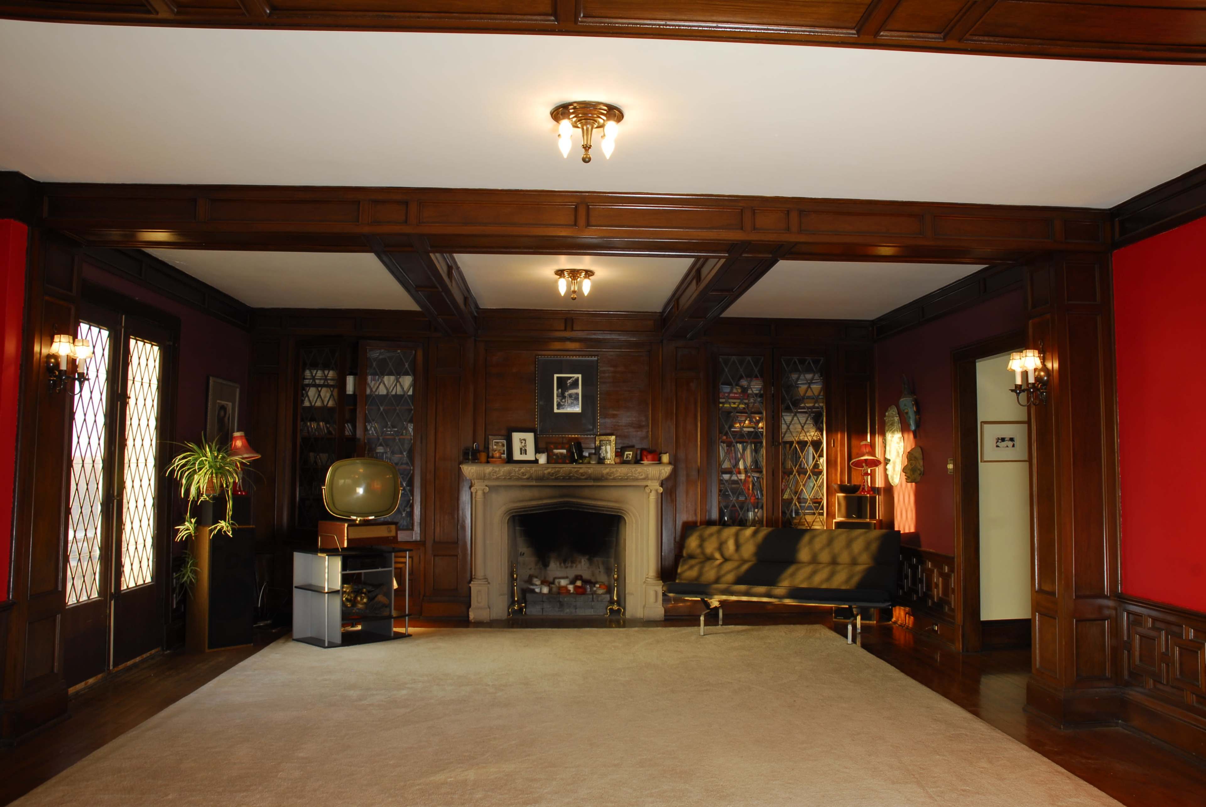 A spacious living room with wooden paneling, a fireplace, a vintage television, and a sofa arranged on a tan carpet.