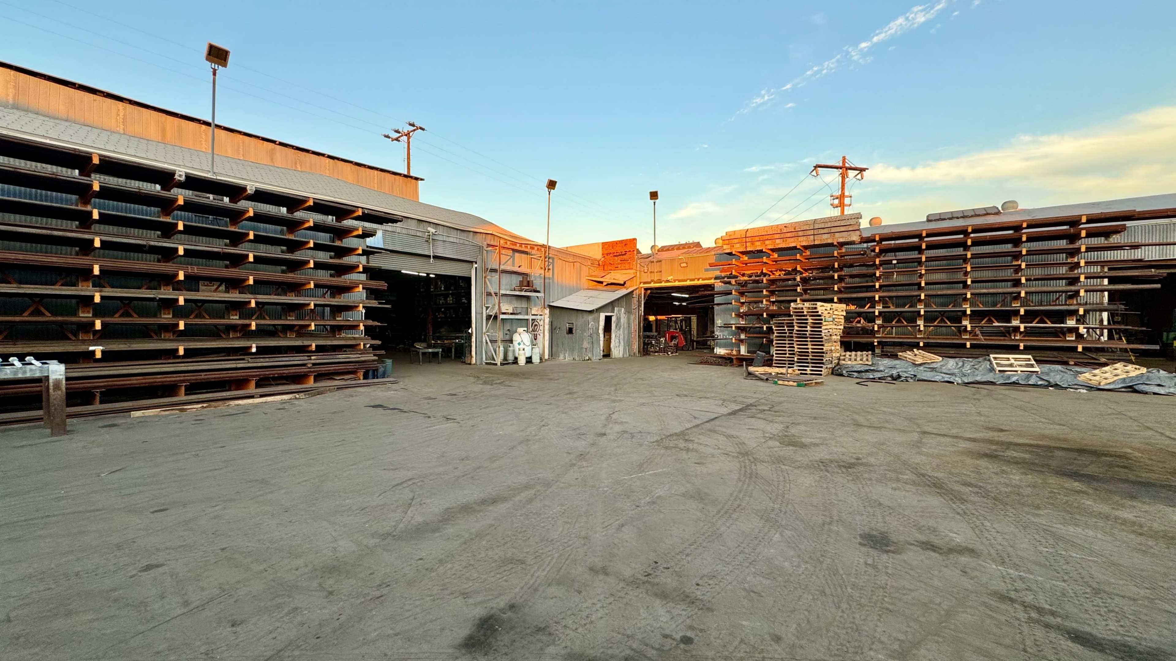 The image shows a large industrial yard with stacked materials and open buildings under a clear sky.