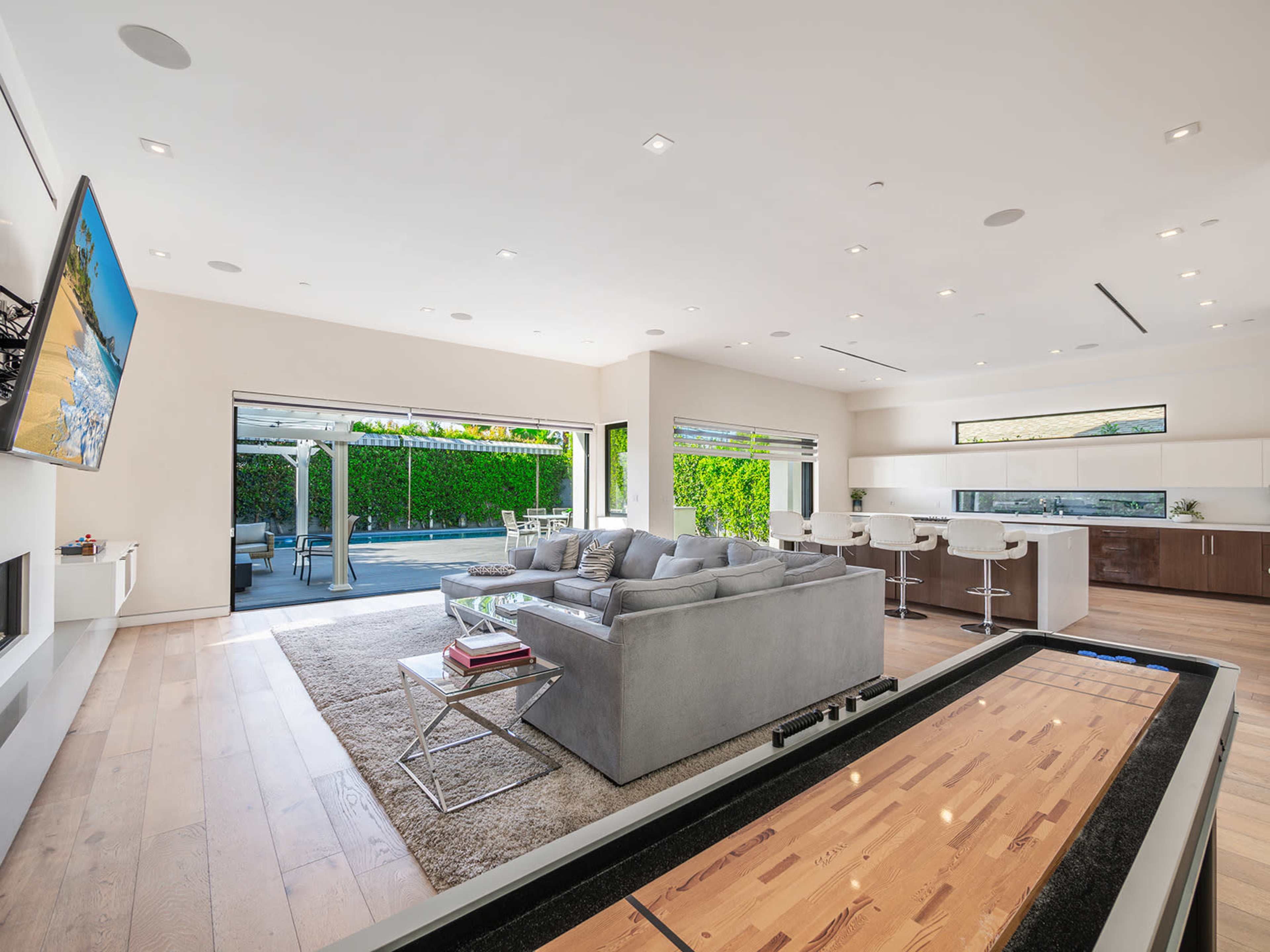 A modern living room with a cozy seating area, a game table, and large windows overlooking an outdoor space with a pool.