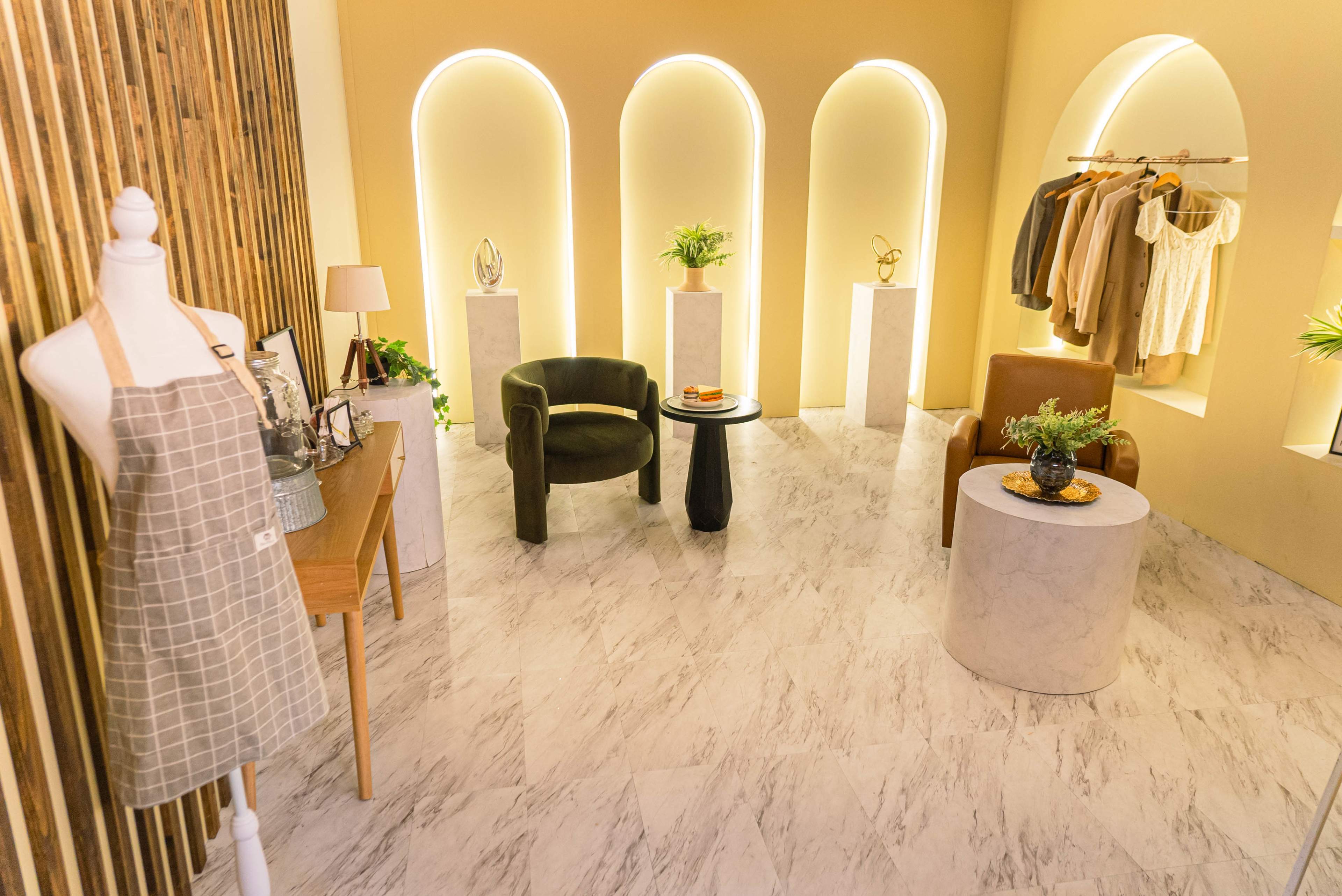The image shows a stylish interior space featuring a mannequin dressed in an apron, two seating areas, and several decorative items on display.