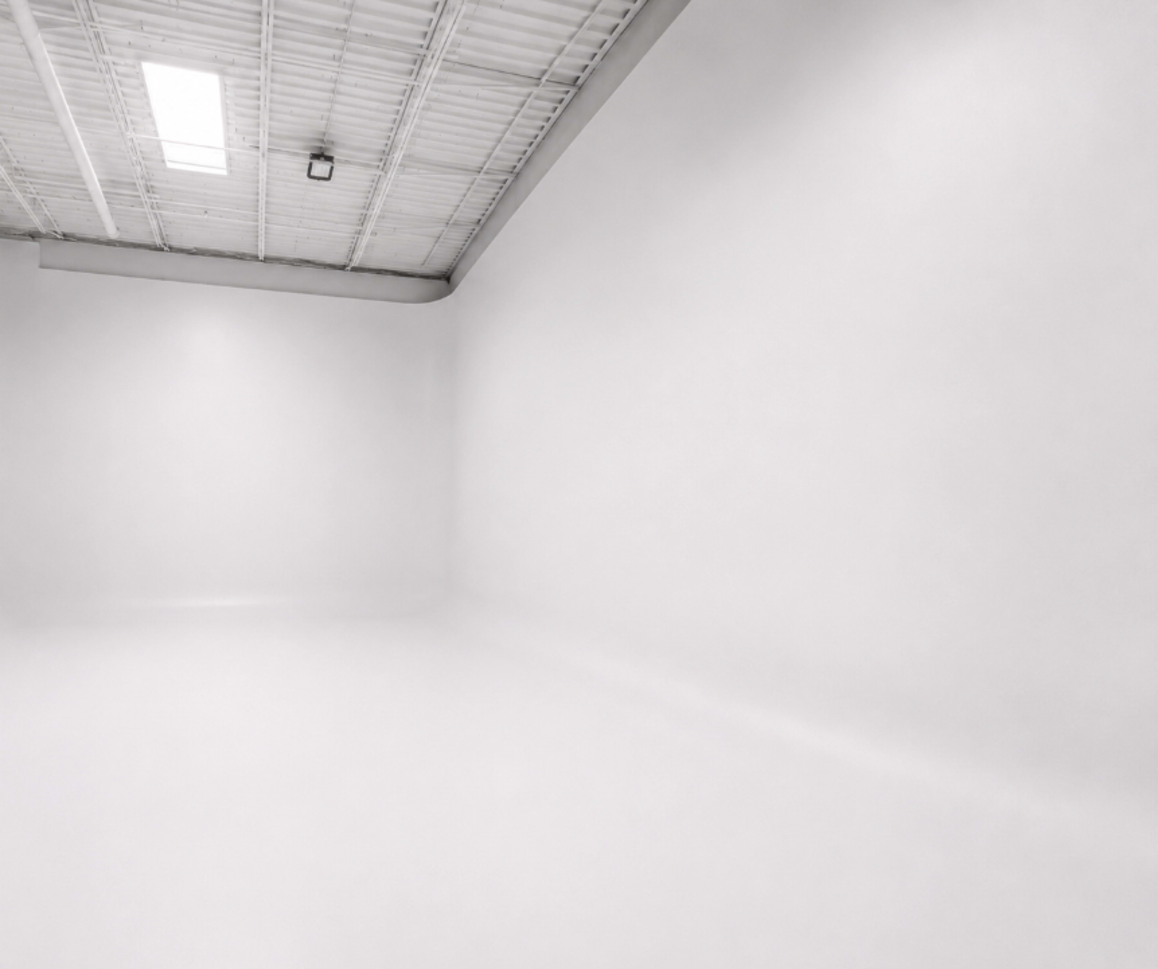 The image shows a spacious, empty room with white walls and a bright, overhead light.