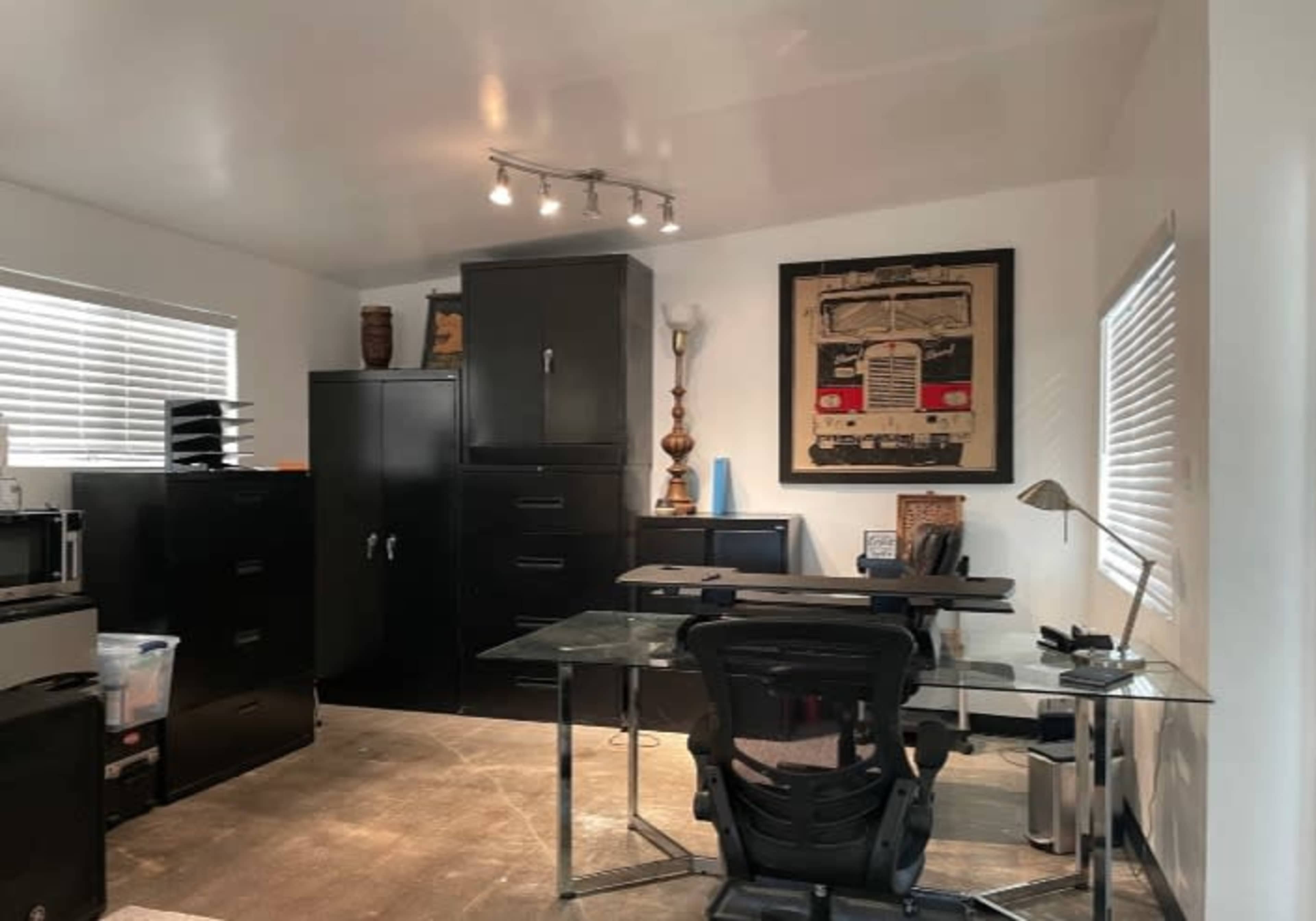 A modern office space features a glass desk, black storage cabinets, and a framed artwork on the wall.