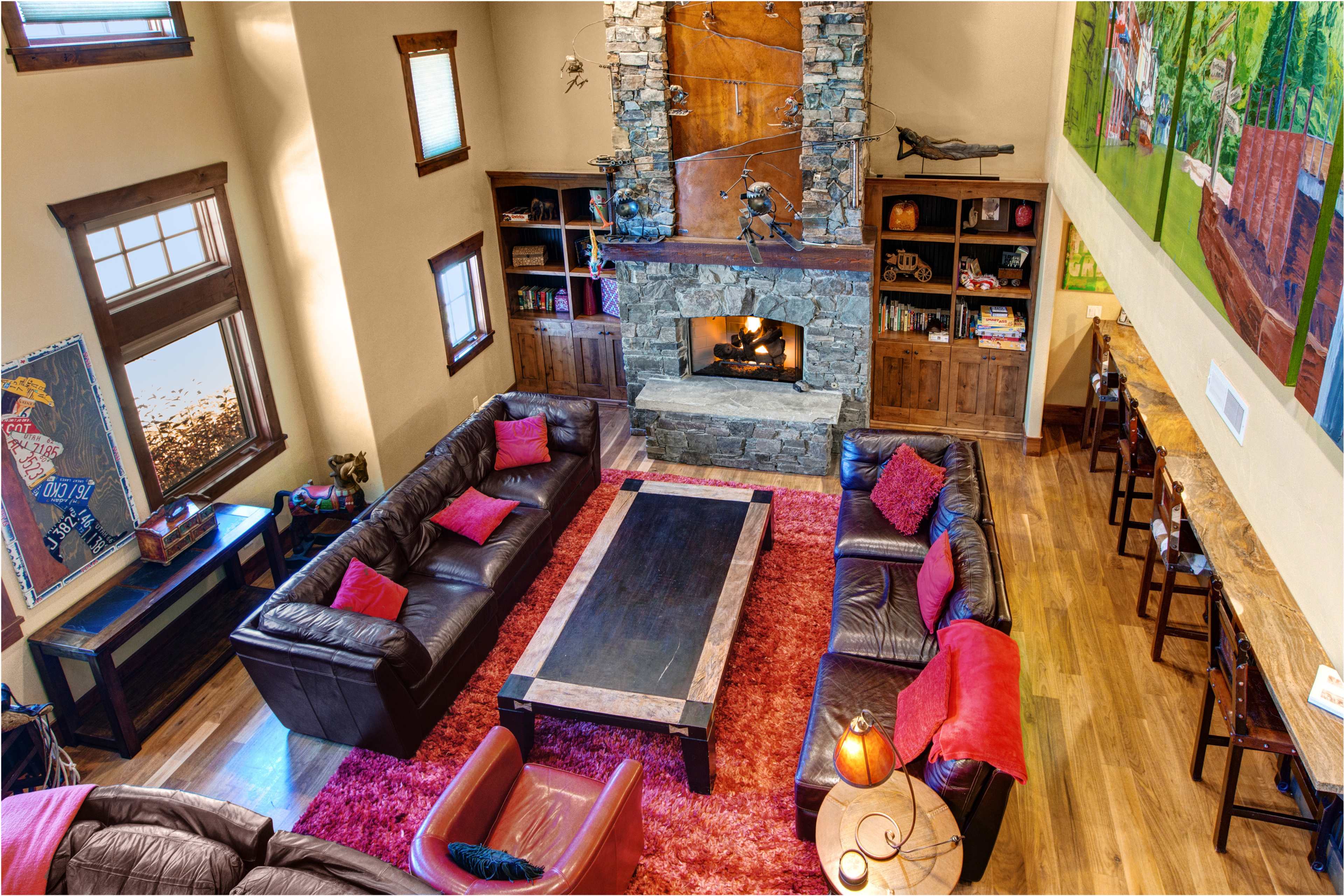 A spacious living room featuring a large stone fireplace, leather sofas arranged around a central coffee table, and a colorful mural on one wall.