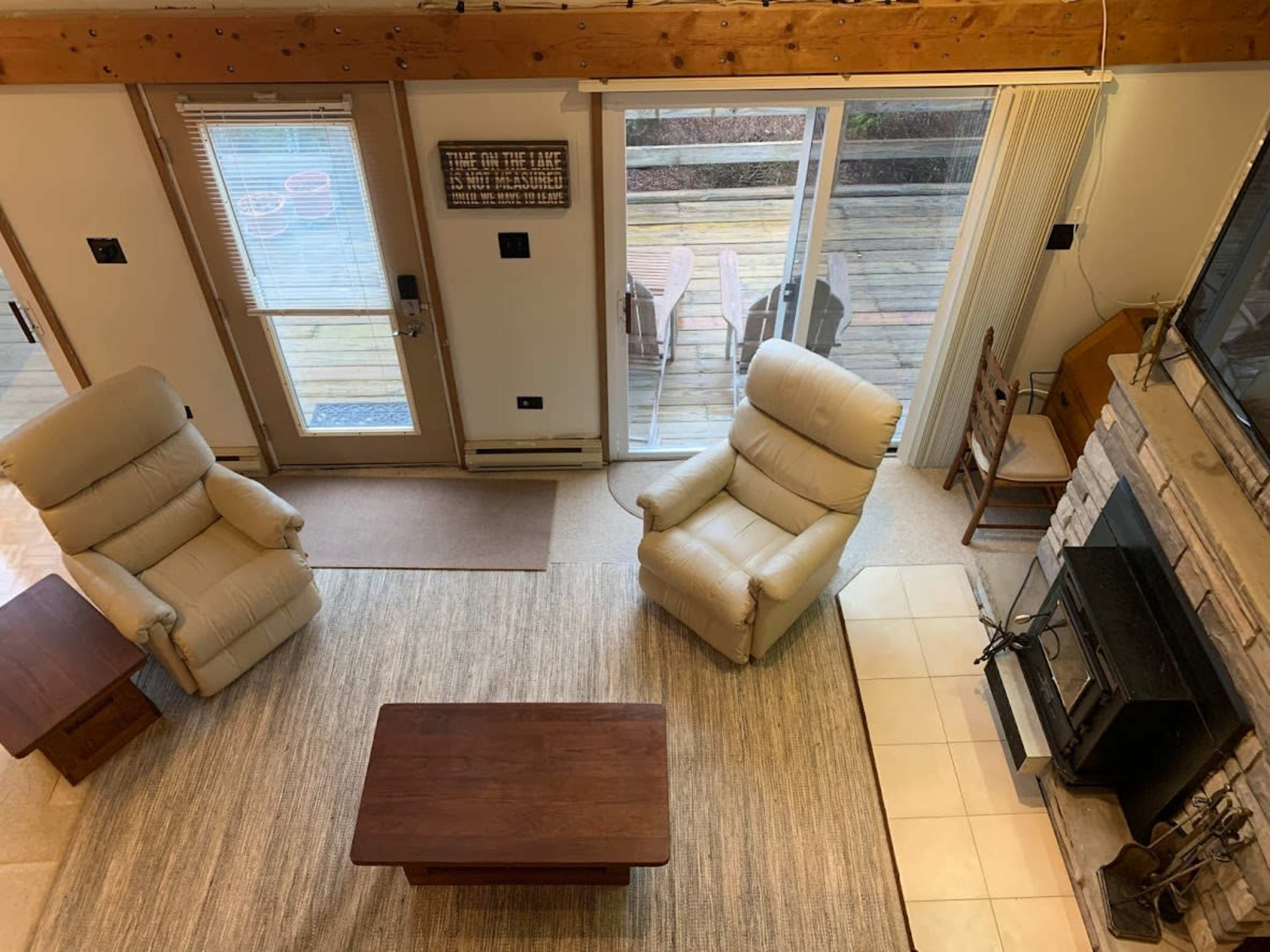 A living room with two upholstered chairs, a wooden coffee table, a stone fireplace, and large windows that open to a deck.
