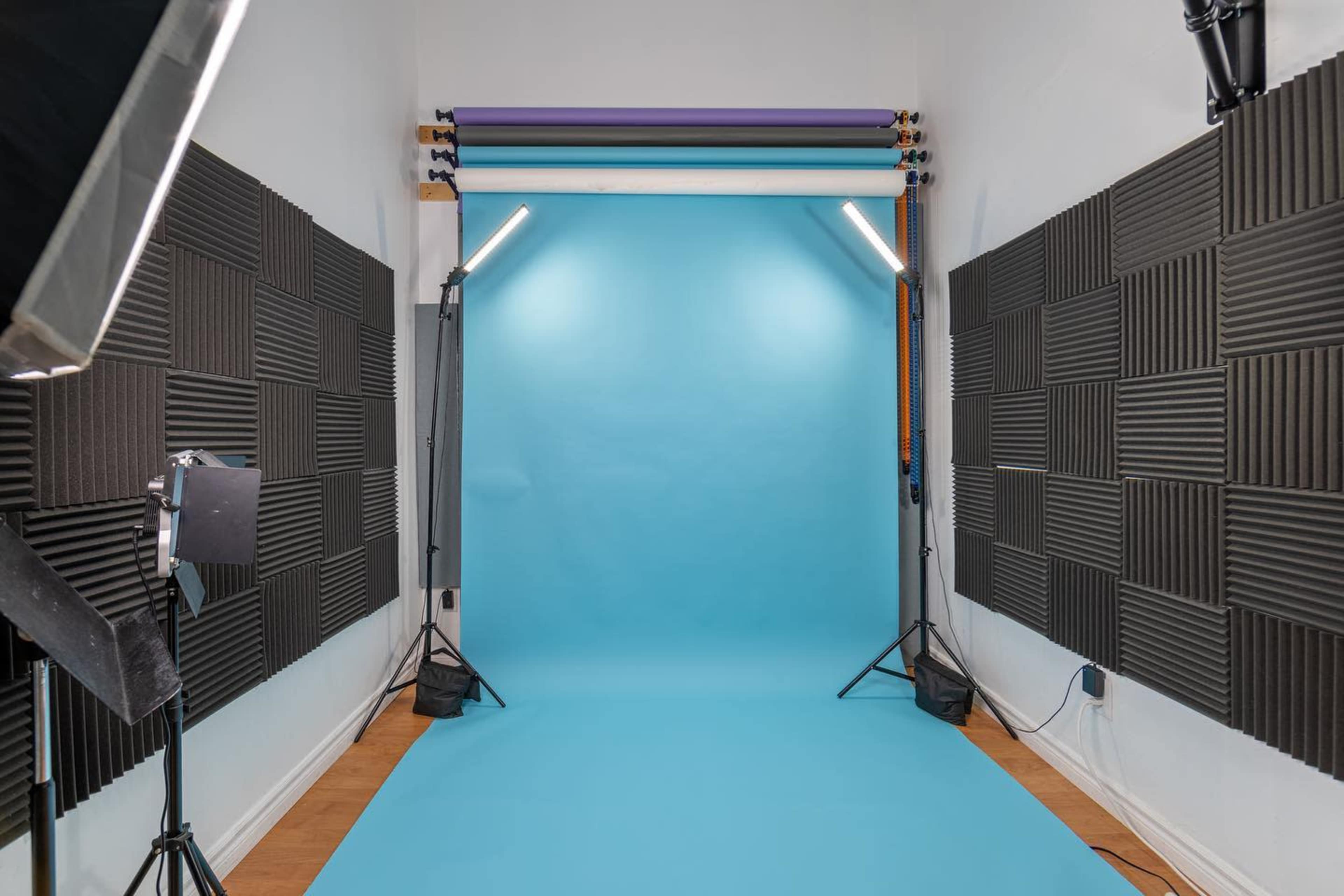 A photography studio with a bright blue backdrop, flanked by soundproofing panels and lighting equipment.