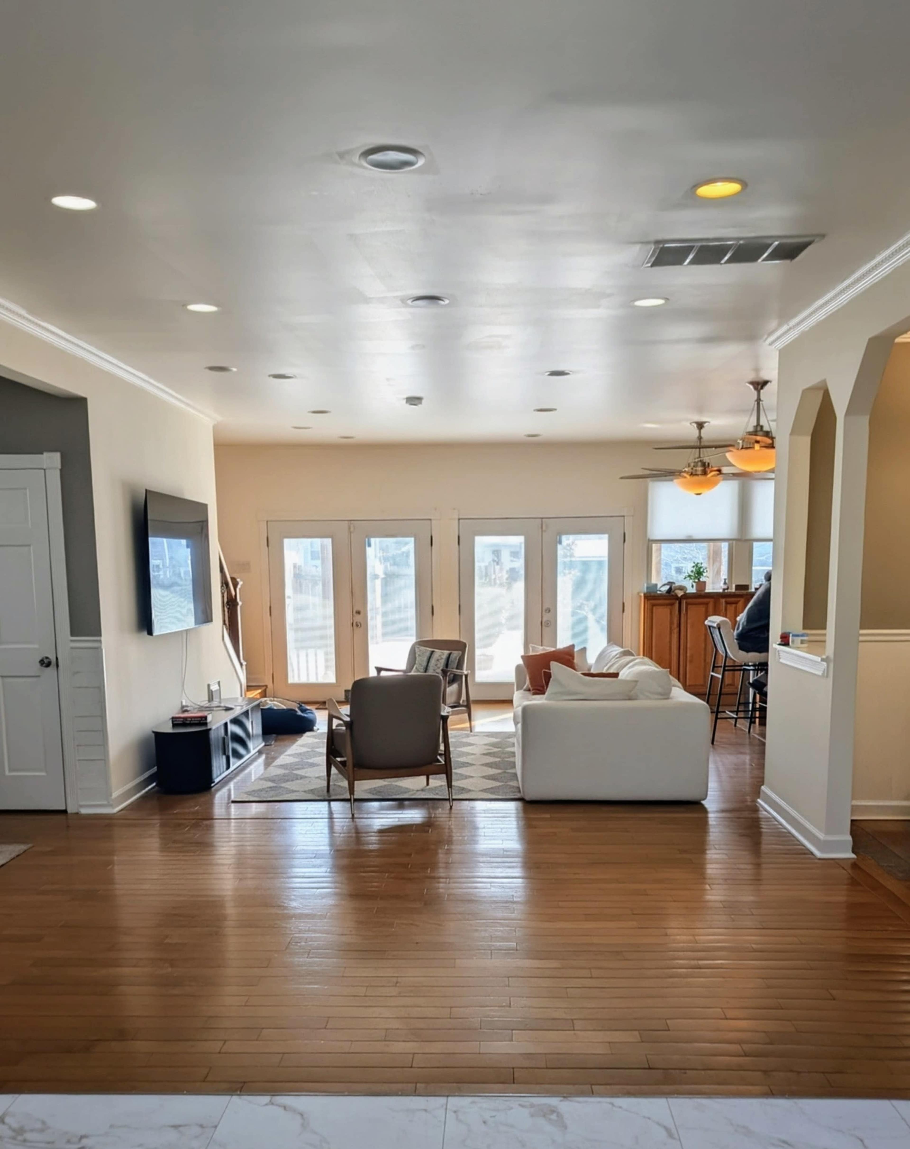 The image shows a modern, open-concept living area with hardwood flooring, a seating area, and large windows leading to a balcony.