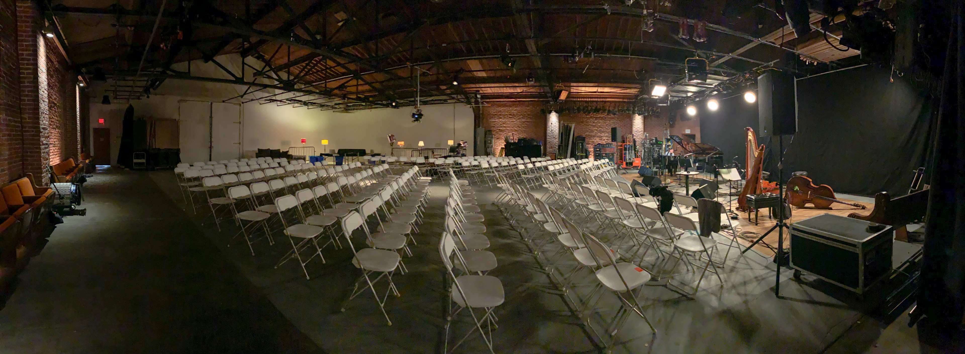 An empty performance space with rows of white chairs arranged facing a stage with musical instruments.