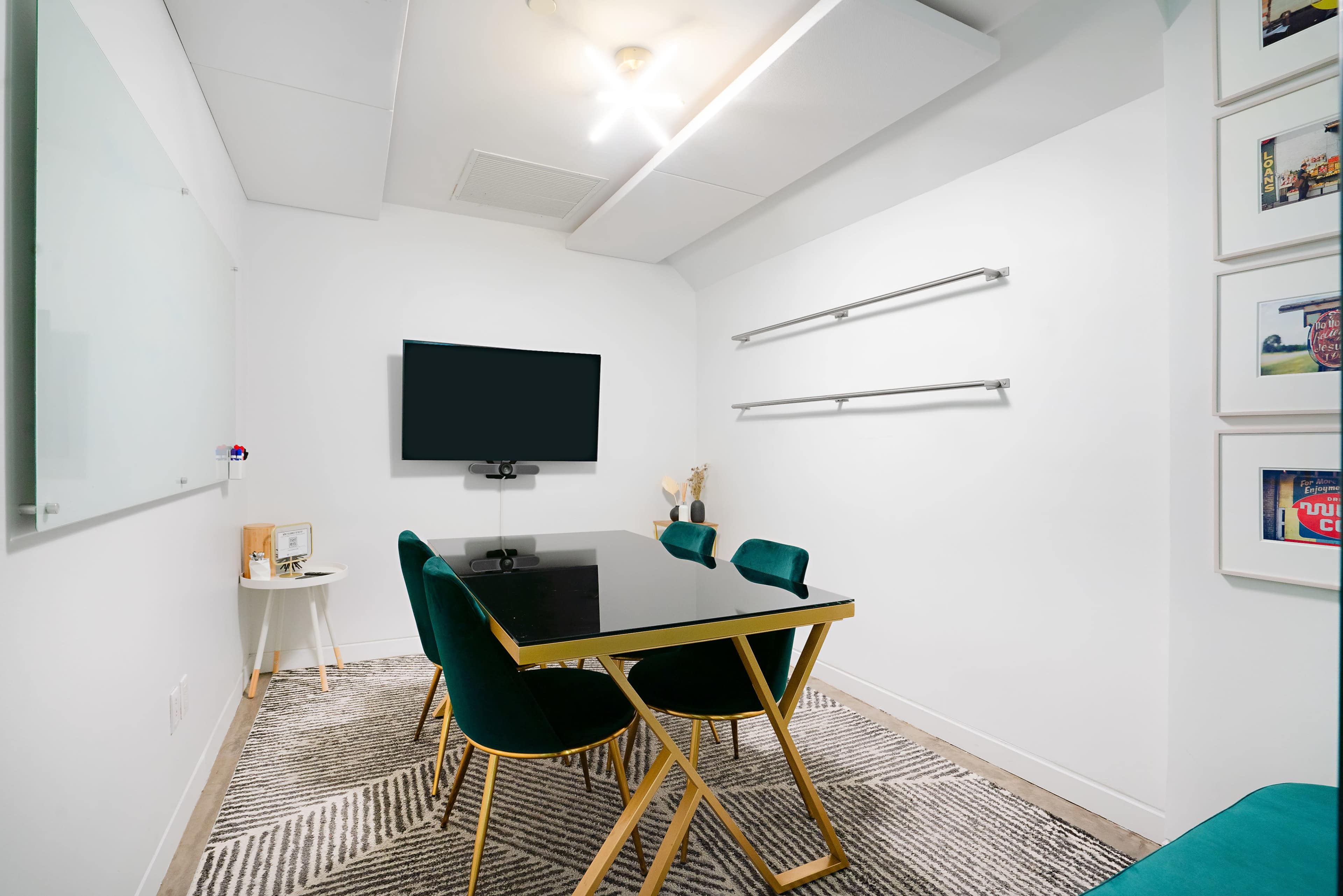 The image shows a modern meeting room featuring a black table surrounded by green chairs, a wall-mounted TV, and a whiteboard.