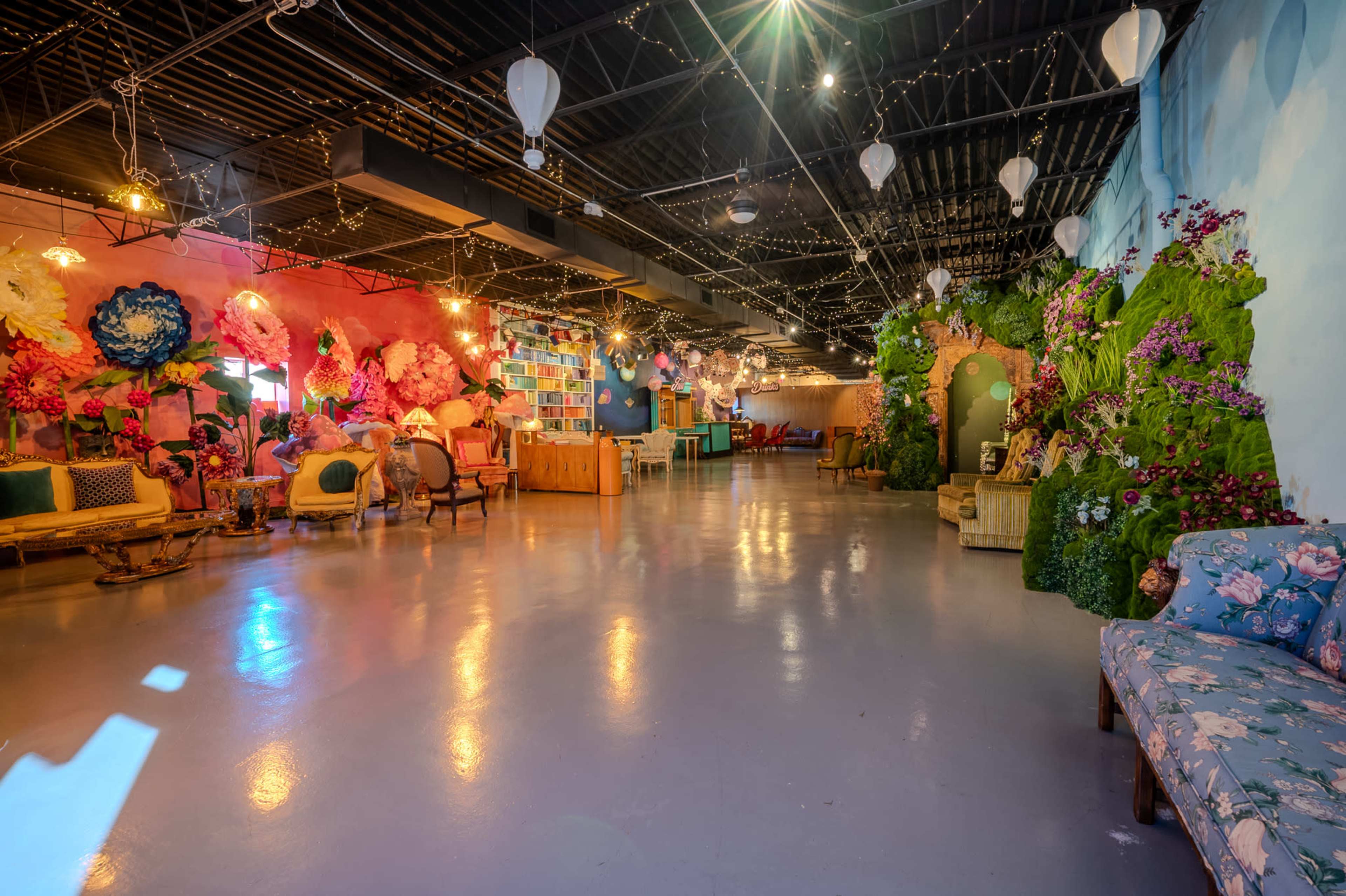 The image shows a spacious, artistically decorated indoor venue with vibrant floral arrangements on the walls and a variety of seating options throughout.