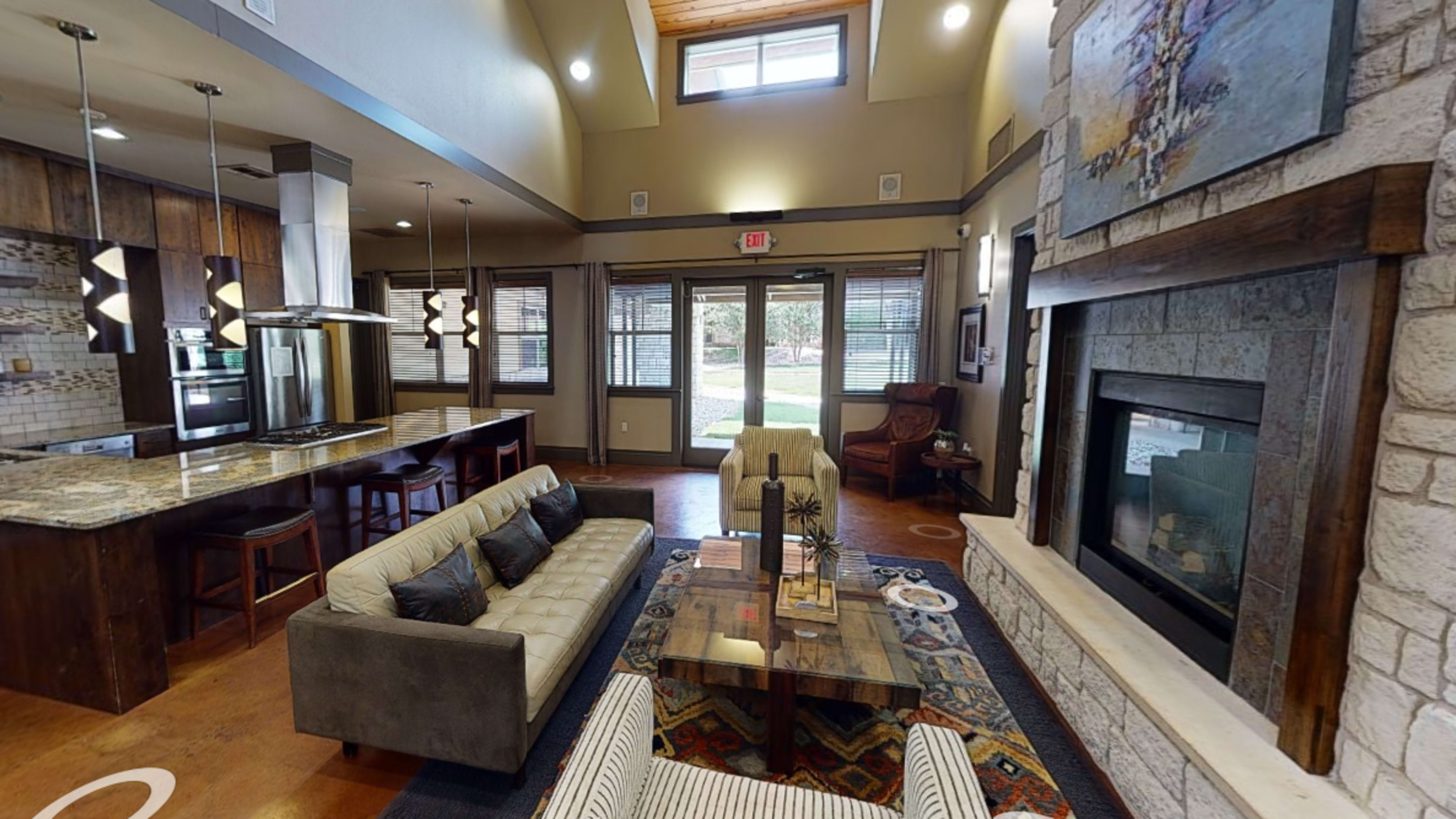 A modern living space with a sectional sofa, a wooden coffee table, a fireplace, and an open kitchen area featuring bar stools and granite countertops.