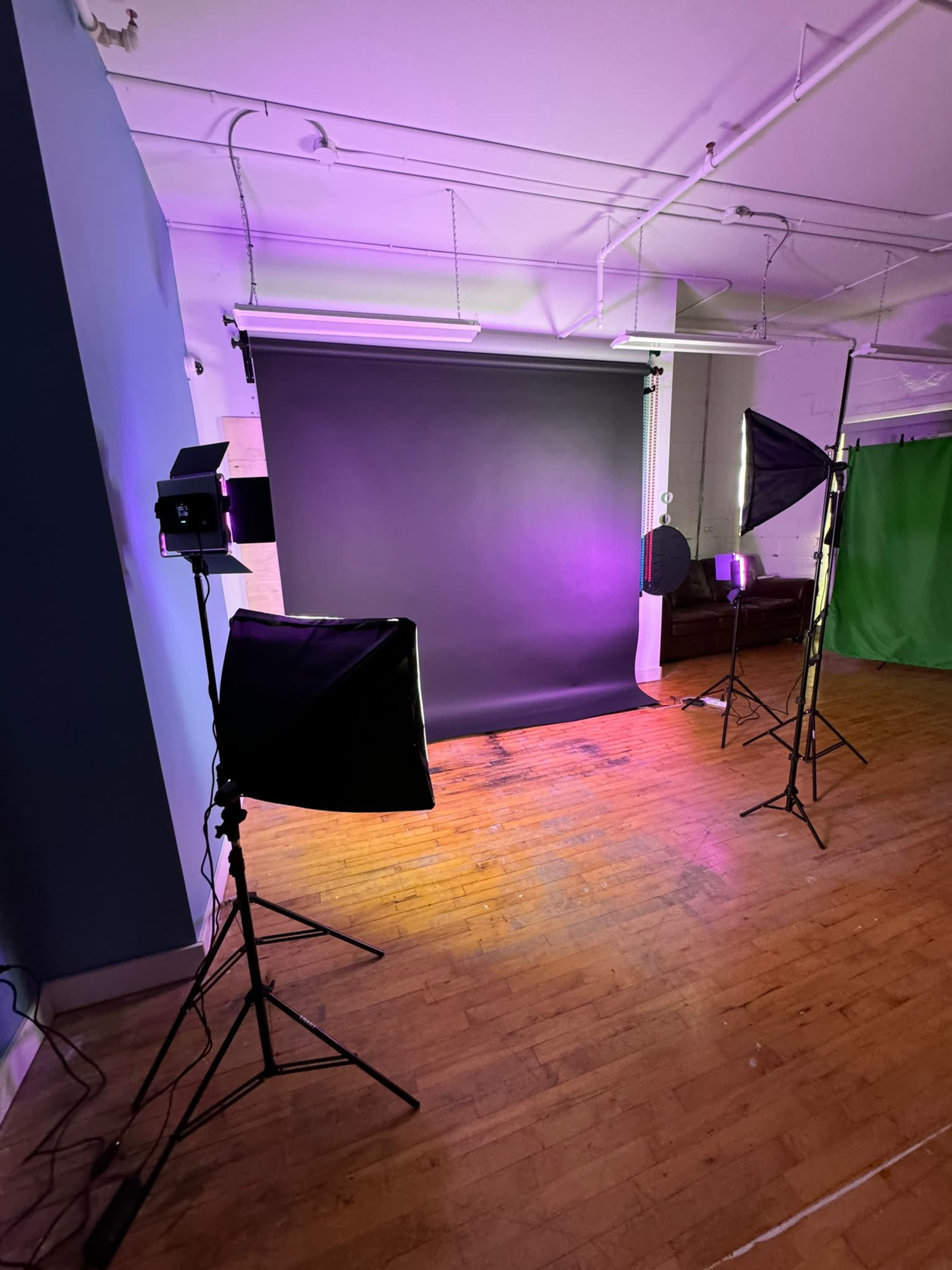 A photo studio setup with a black backdrop, three light stands, and a green screen in the background.