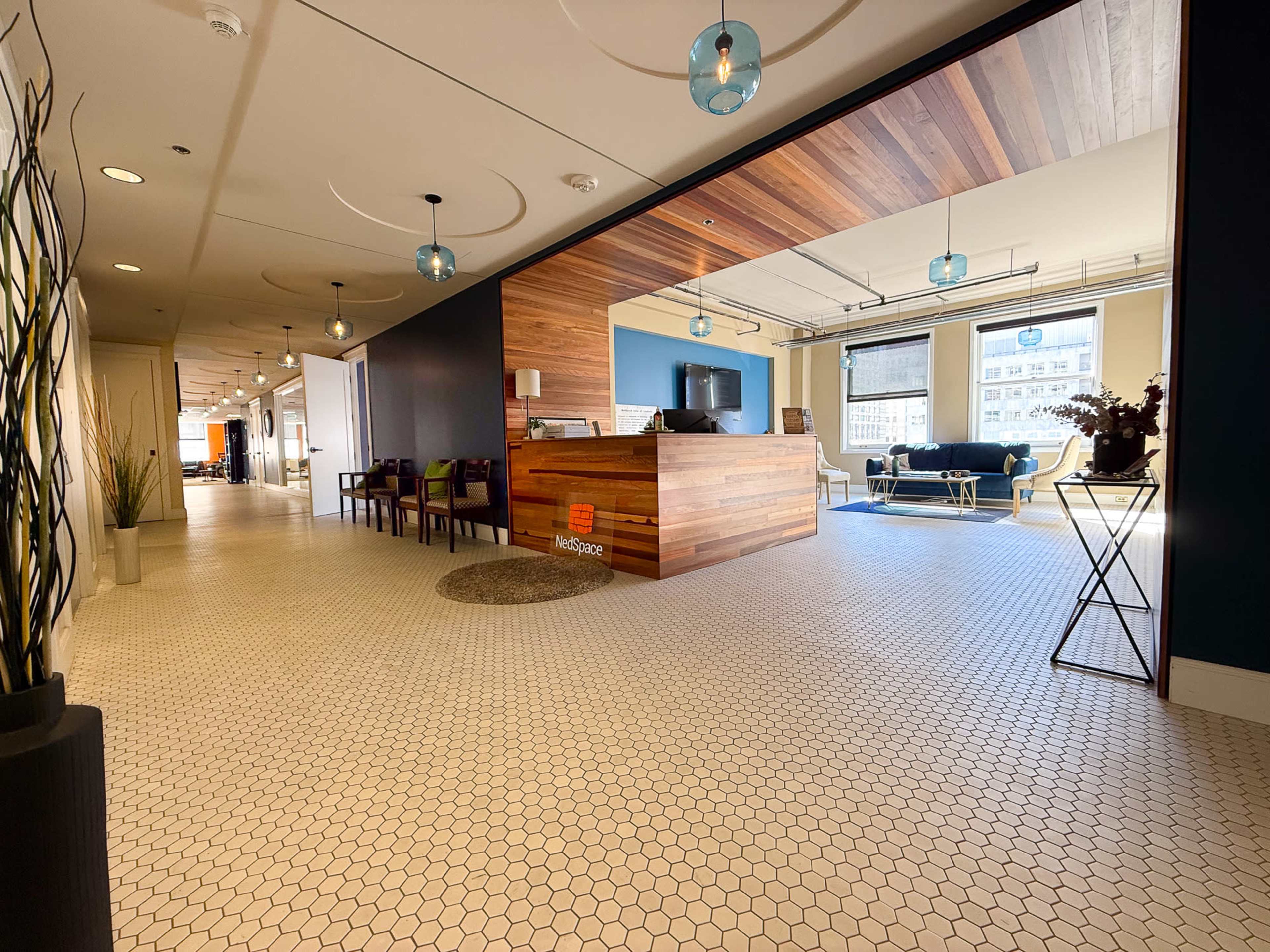 The image shows a modern office reception area featuring a wooden front desk, seating arrangements, and hexagonal tiled flooring.