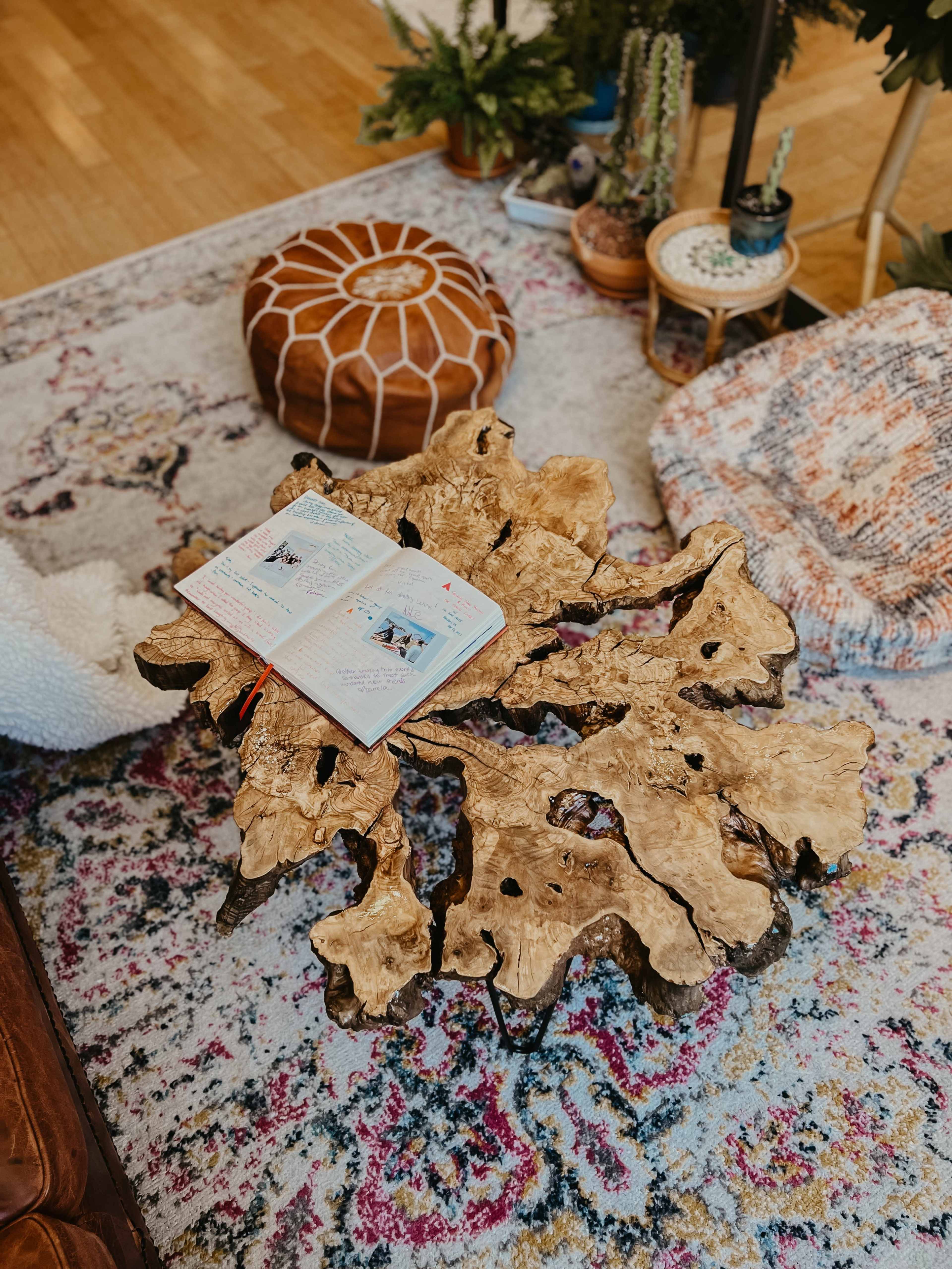 A wooden coffee table with a unique organic shape holds an open notebook on a colorful patterned rug in a cozy living space.