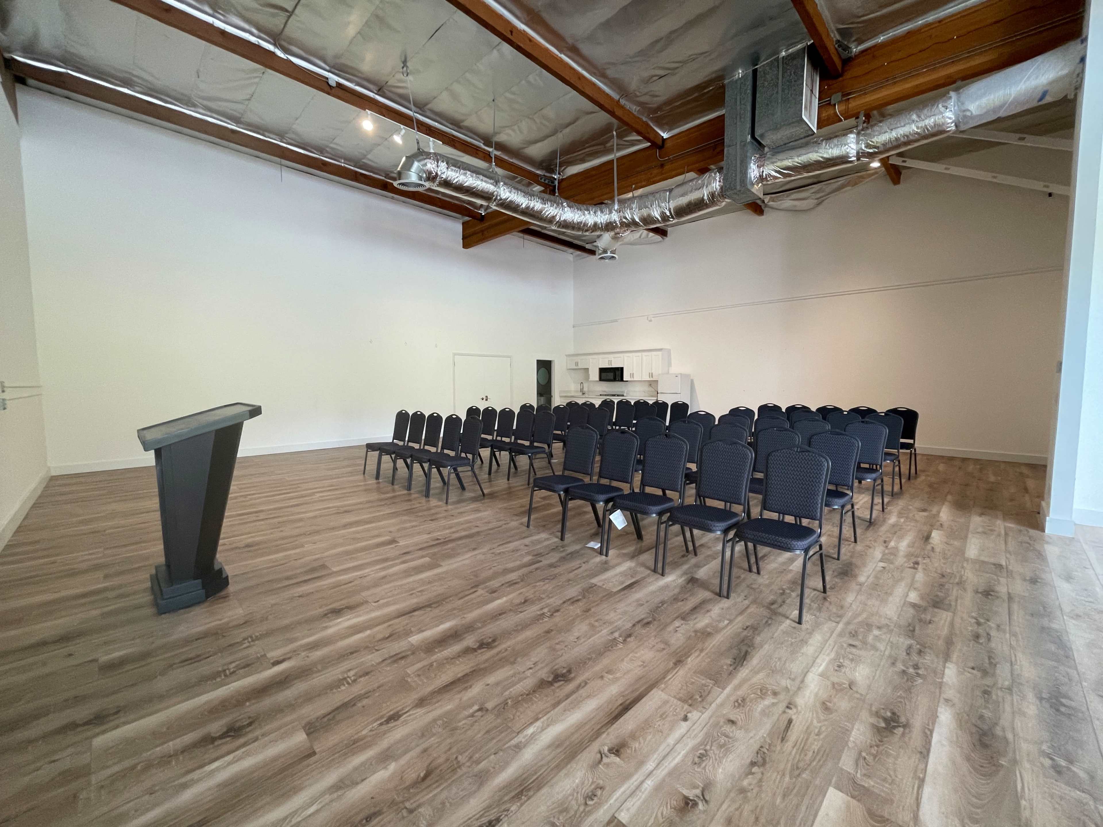 A spacious room with a podium at the front and rows of black chairs set up for an audience.