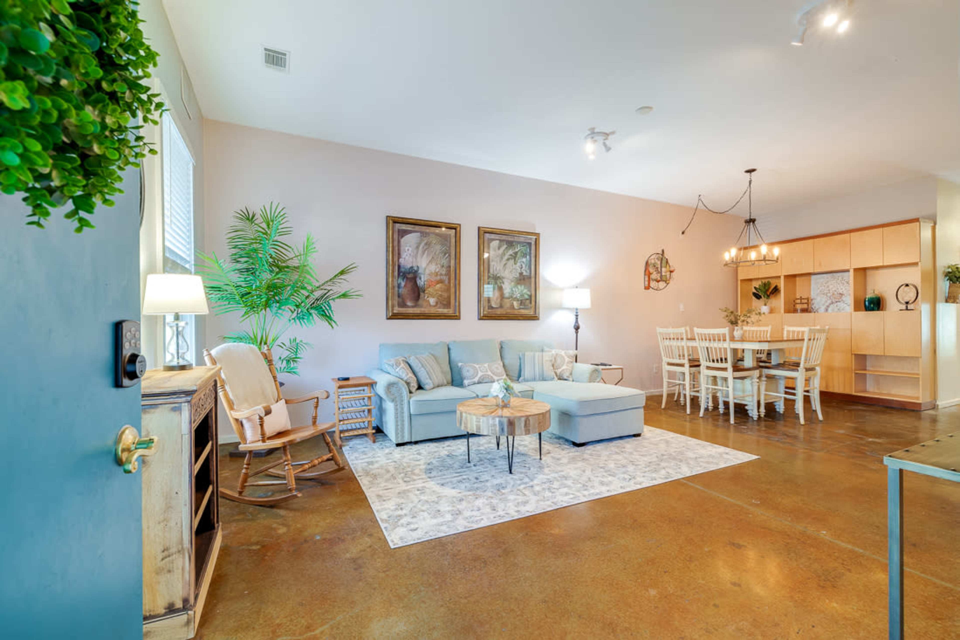 The room features a light blue seating area with a coffee table, a rocking chair, and a dining space with a wooden table and chairs.