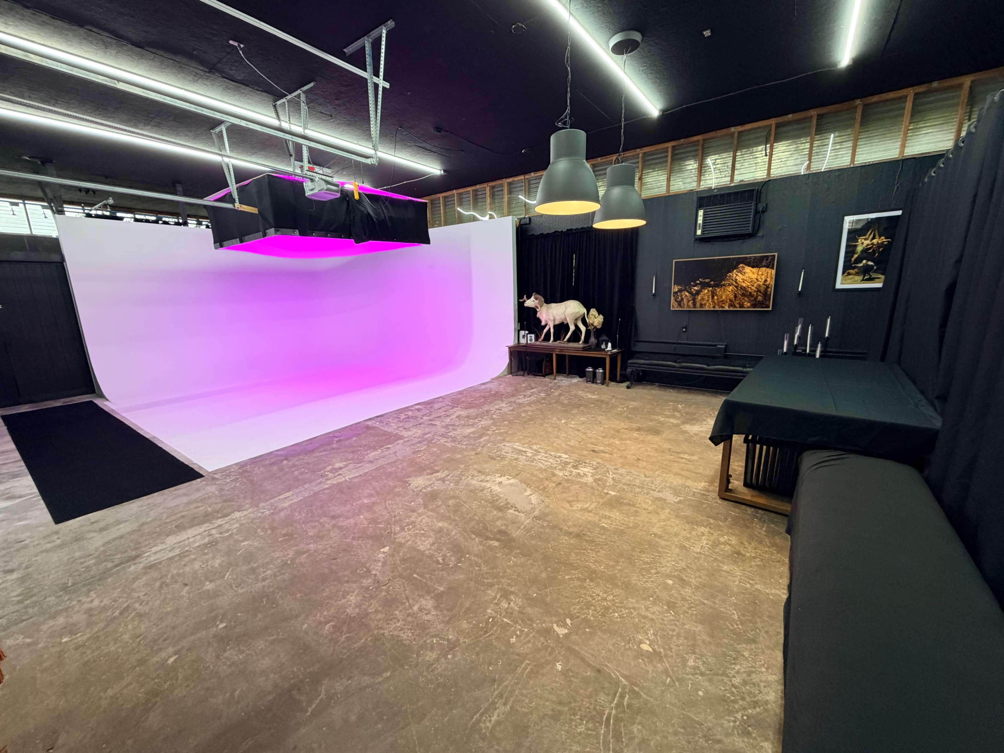 The image shows a photo studio with a large white backdrop illuminated by pink lights, black curtains, and a table with decorations in the foreground.