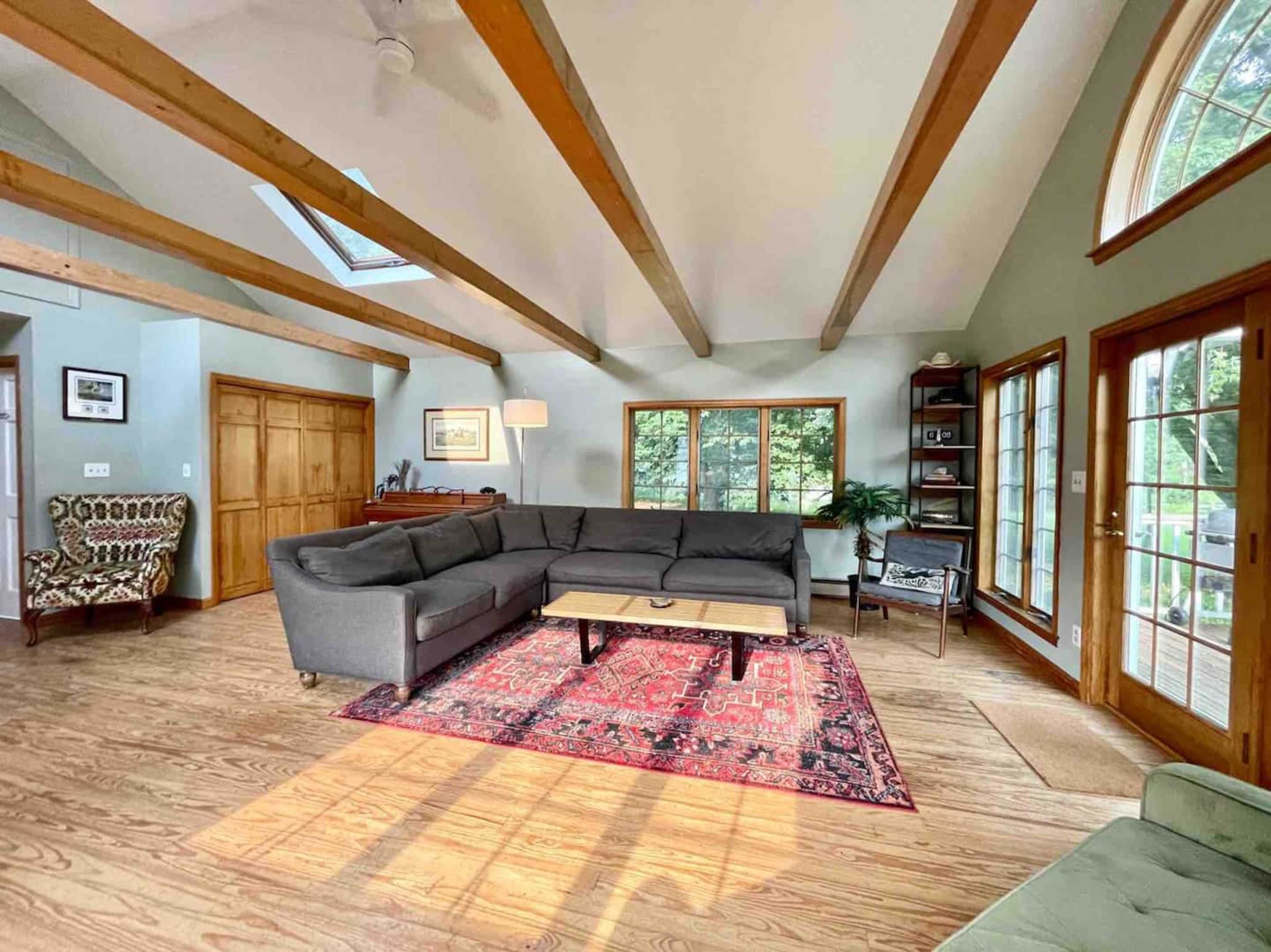 A spacious living room features a gray sectional sofa, a coffee table on a patterned rug, and large windows providing natural light.